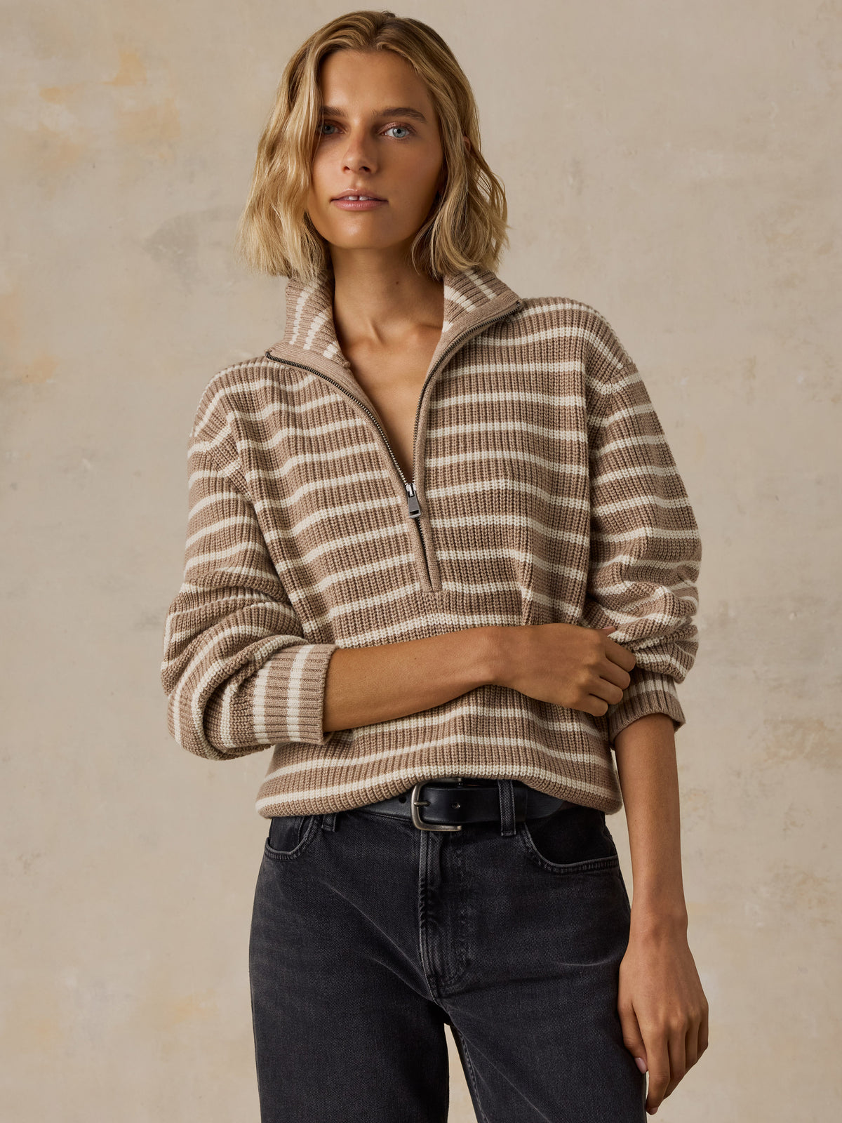 A woman wearing a beige and brown striped quarter-zip pullover sweater with dark wash jeans, image 1 of 5