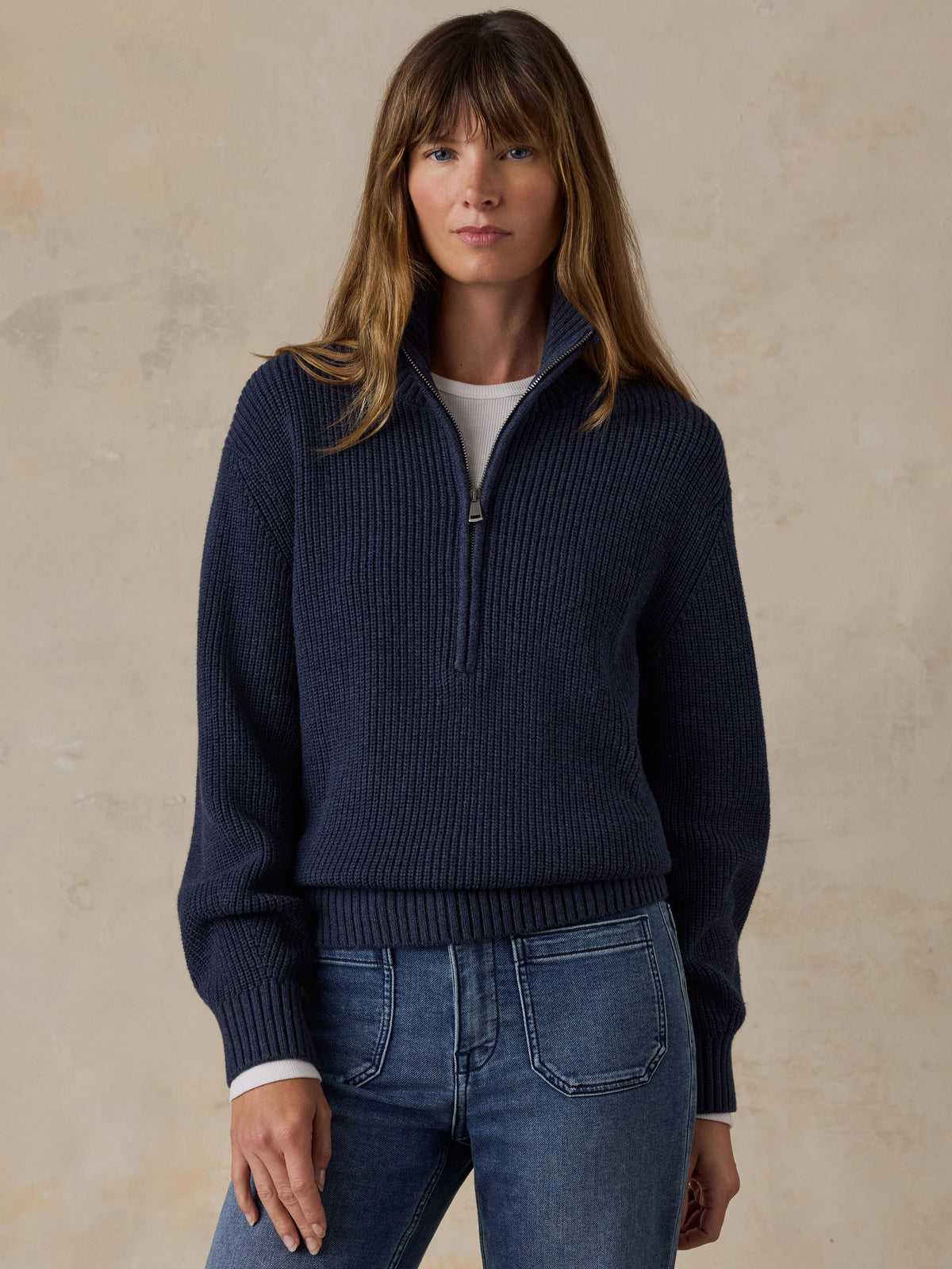 Woman wearing a navy blue quarter zip sweater and blue jeans, image 1 of 6