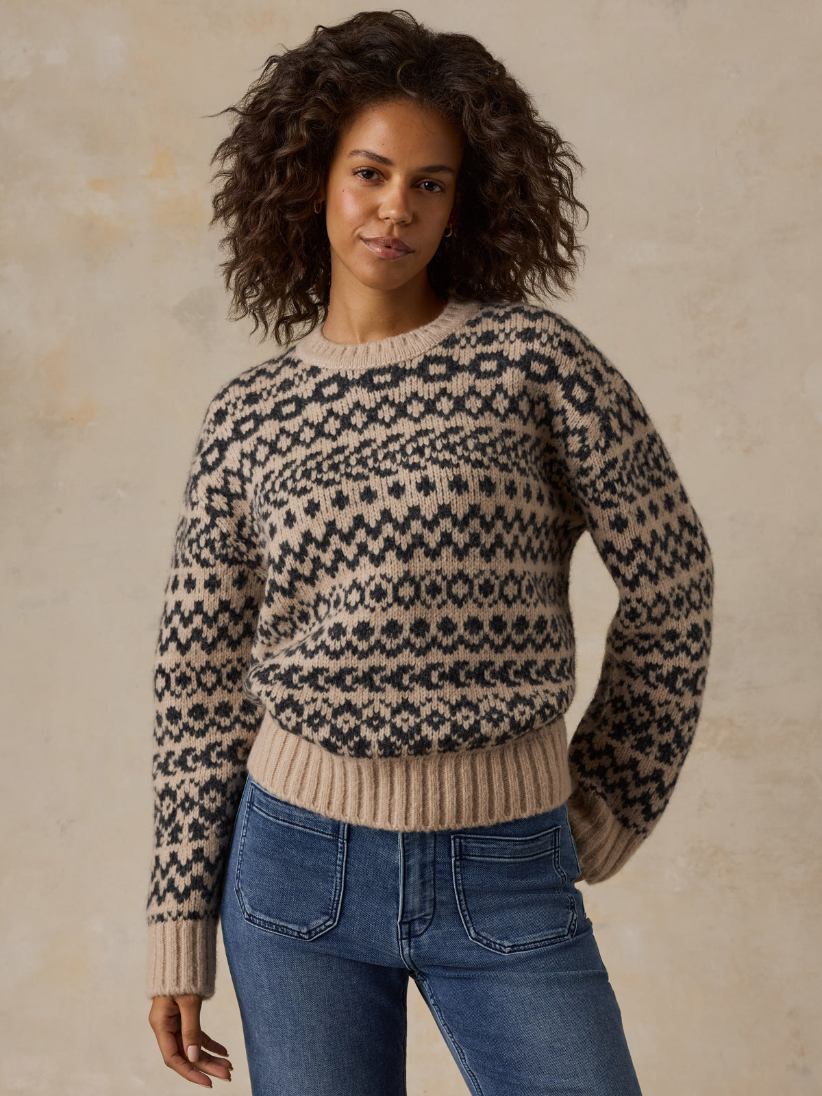 A woman wearing a beige printed sweater and blue jeans, image 7 of 7