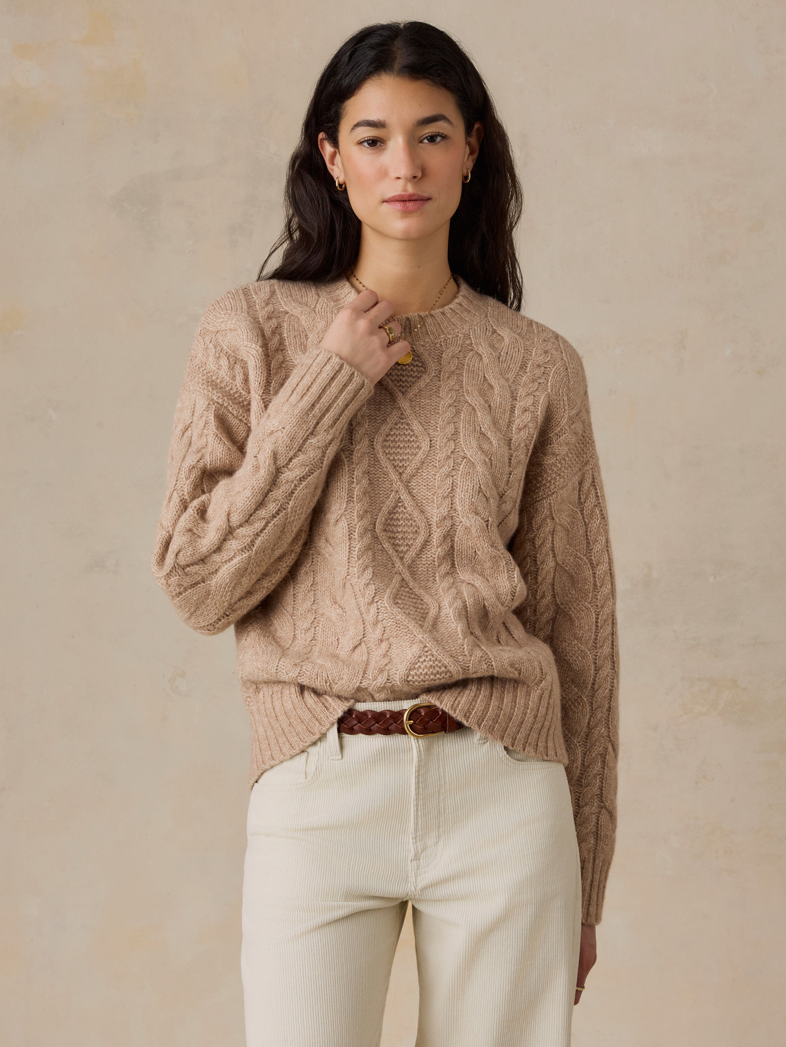 A woman wearing a beige sweater and white pants
