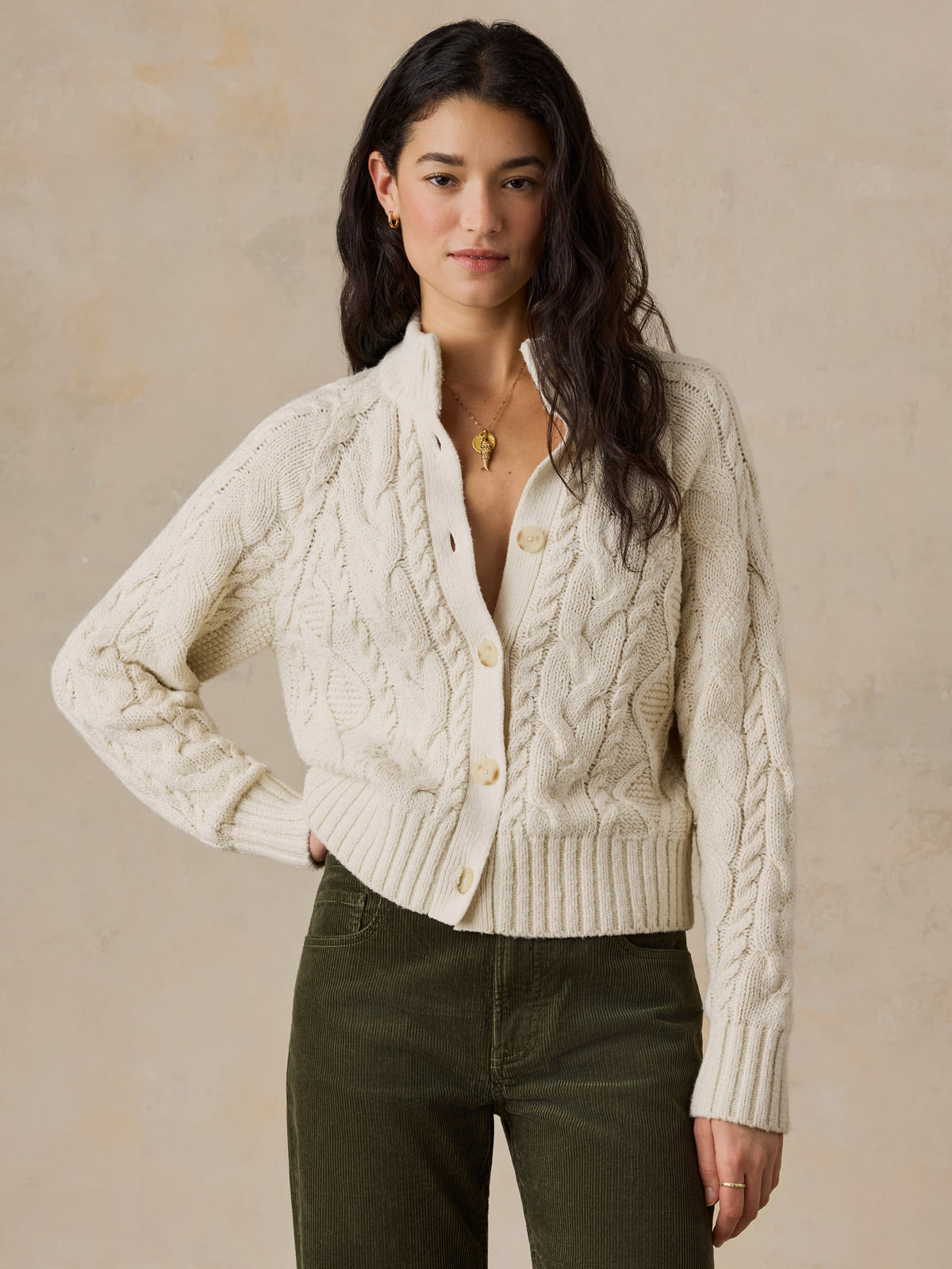 A woman wearing a cream cardigan and green pants, image 1 of 7