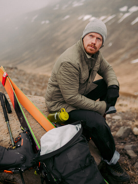Man sitting next to his ski kit wearing a quilted CPO jacket