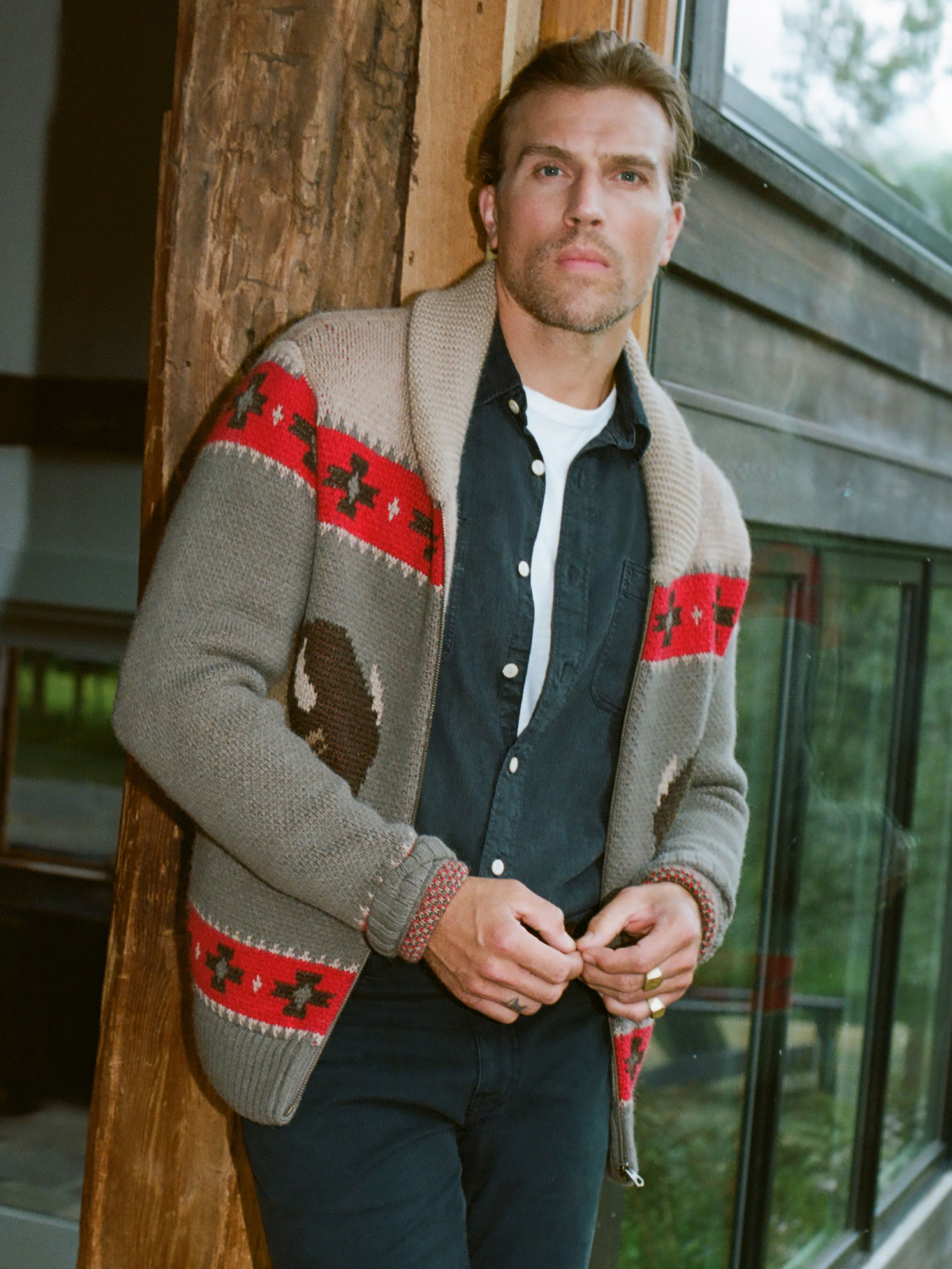 Man wearing a patterned cardigan standing outside of a house