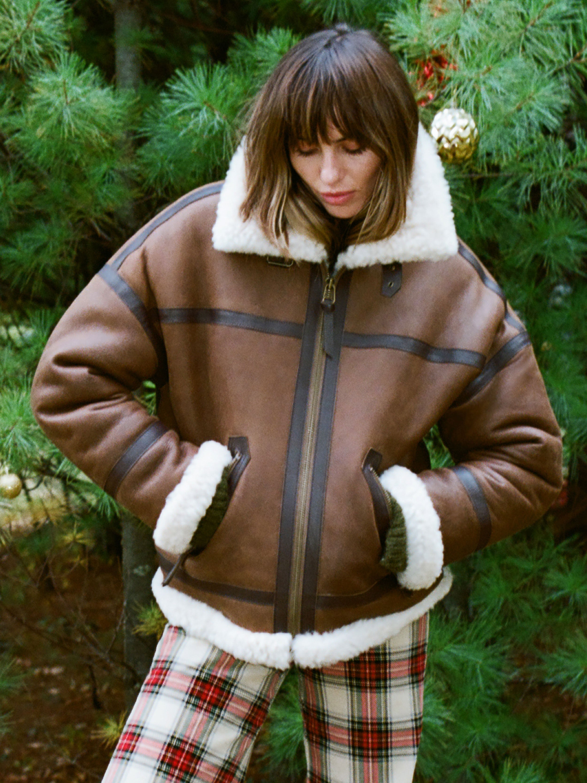 Woman is wearing a brown shearling jacket against a beige background