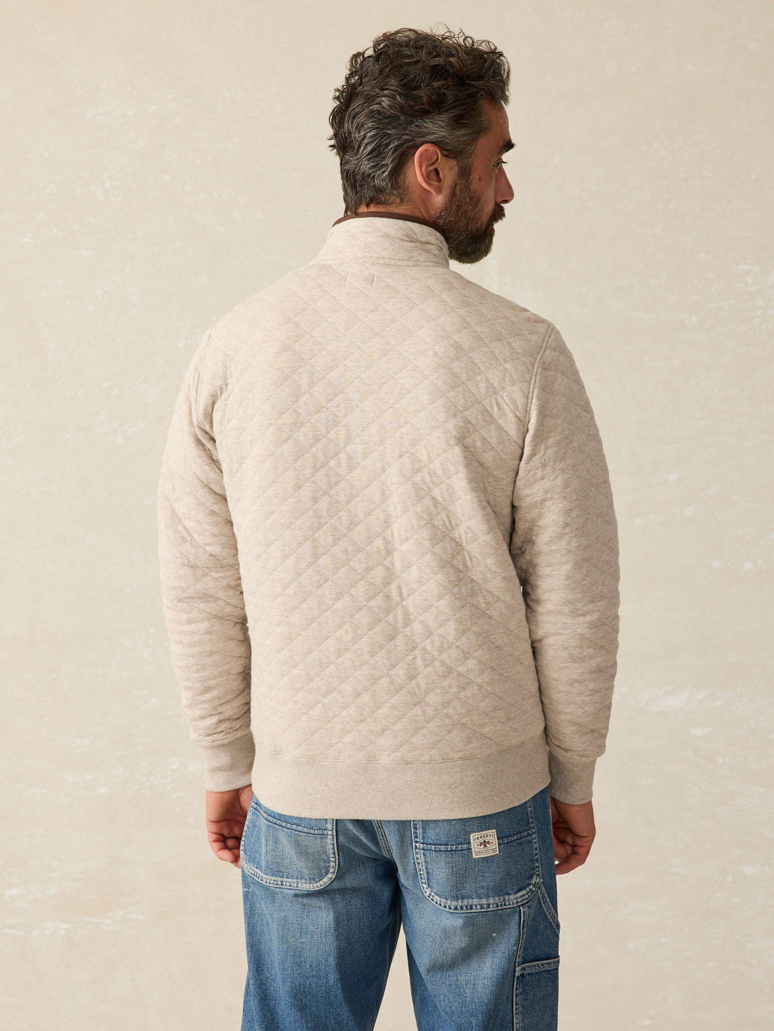 Man wearing an oatmeal quilted pullover sweater with blue jeans against a beige background