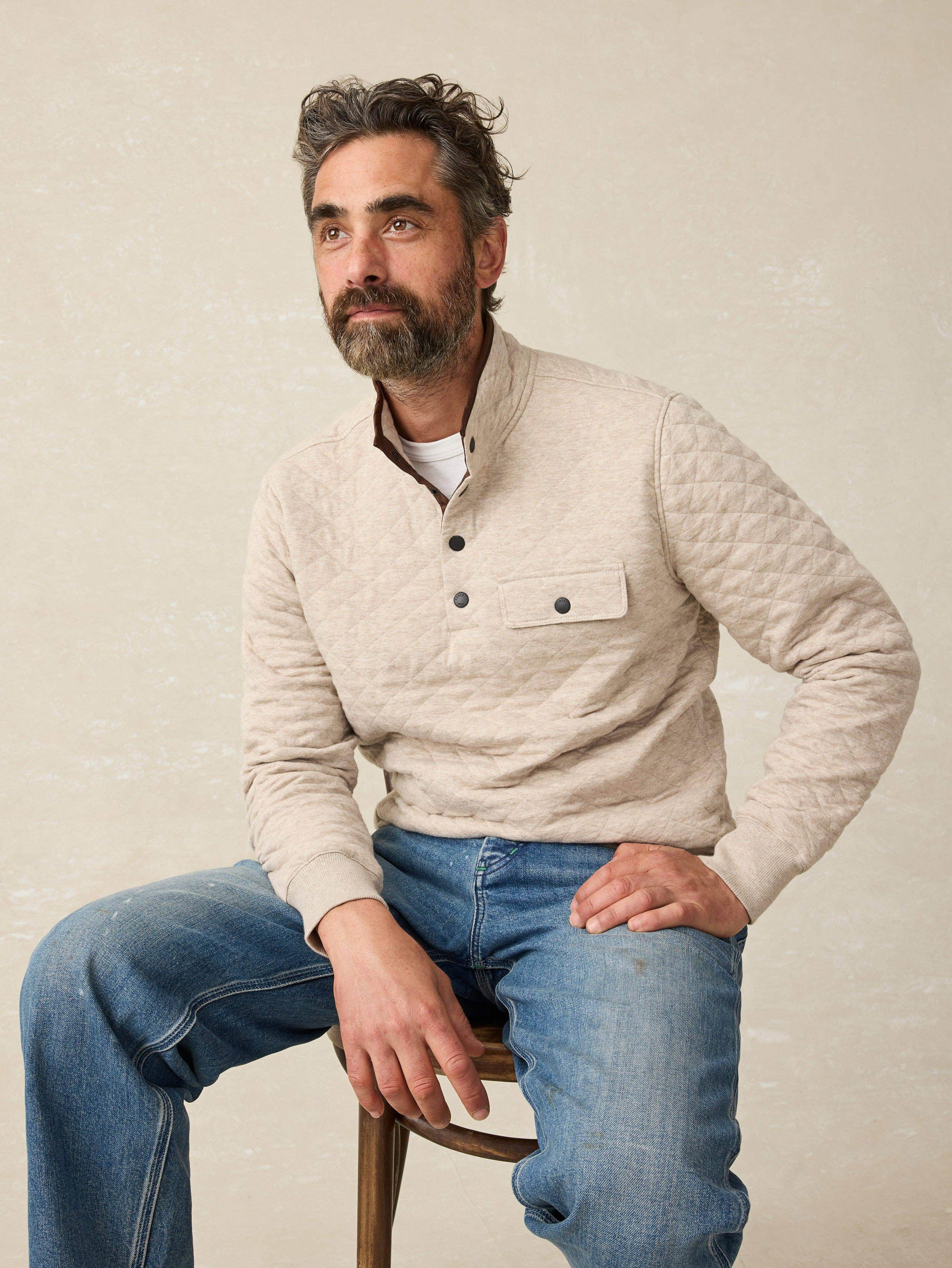 Man wearing an oatmeal quilted pullover sweater with blue jeans against a beige background