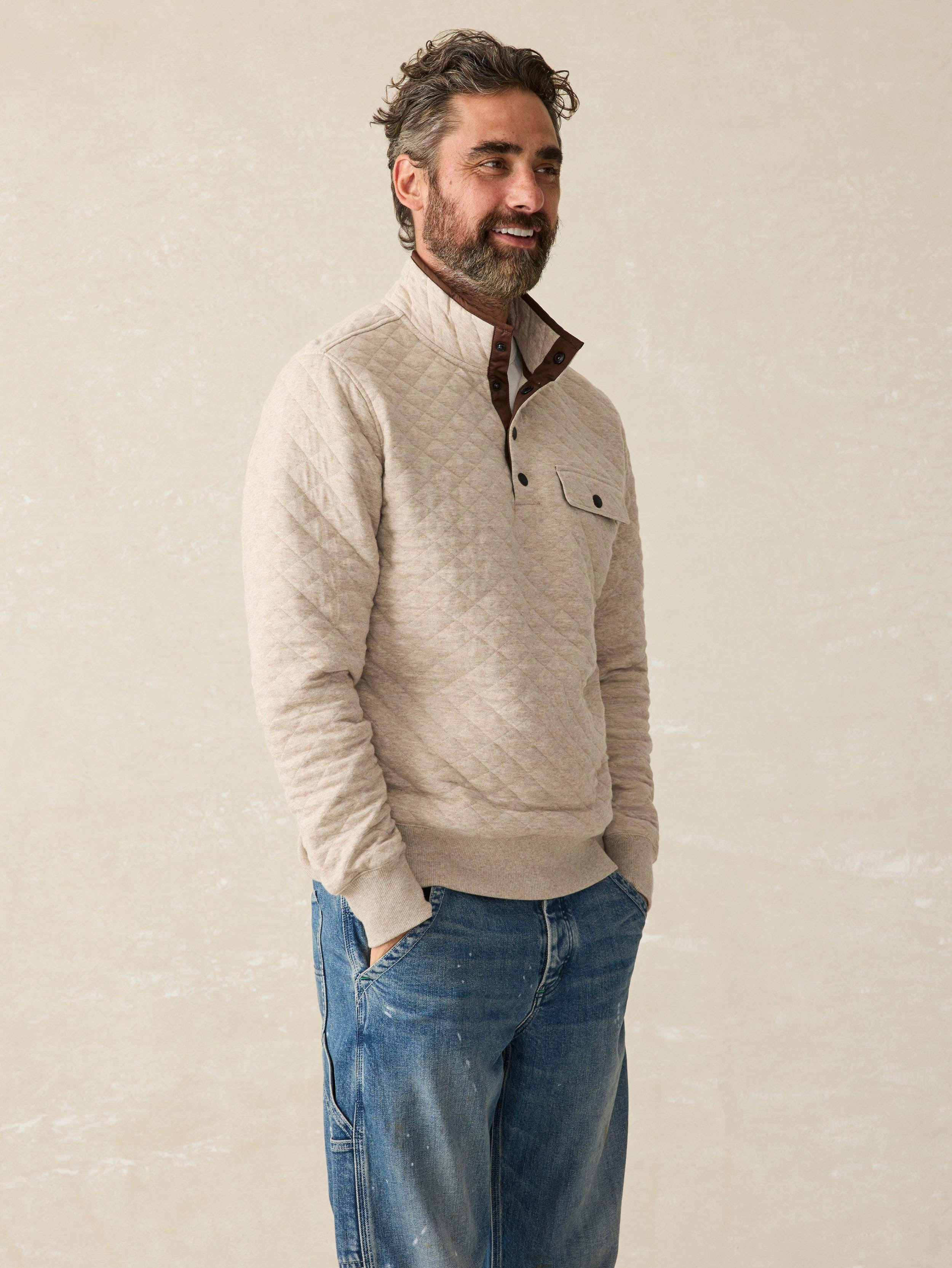 Man wearing an oatmeal quilted pullover sweater with blue jeans against a beige background
