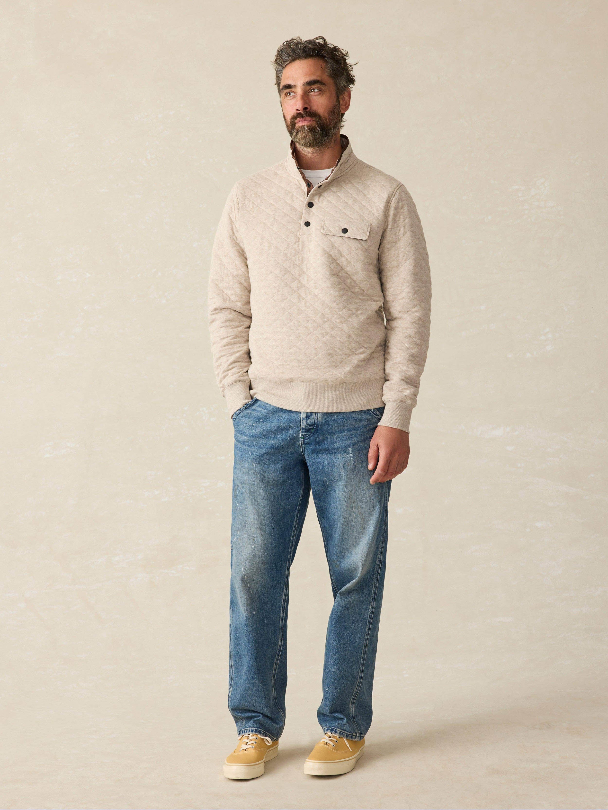 Man wearing an oatmeal quilted pullover sweater with blue jeans against a beige background