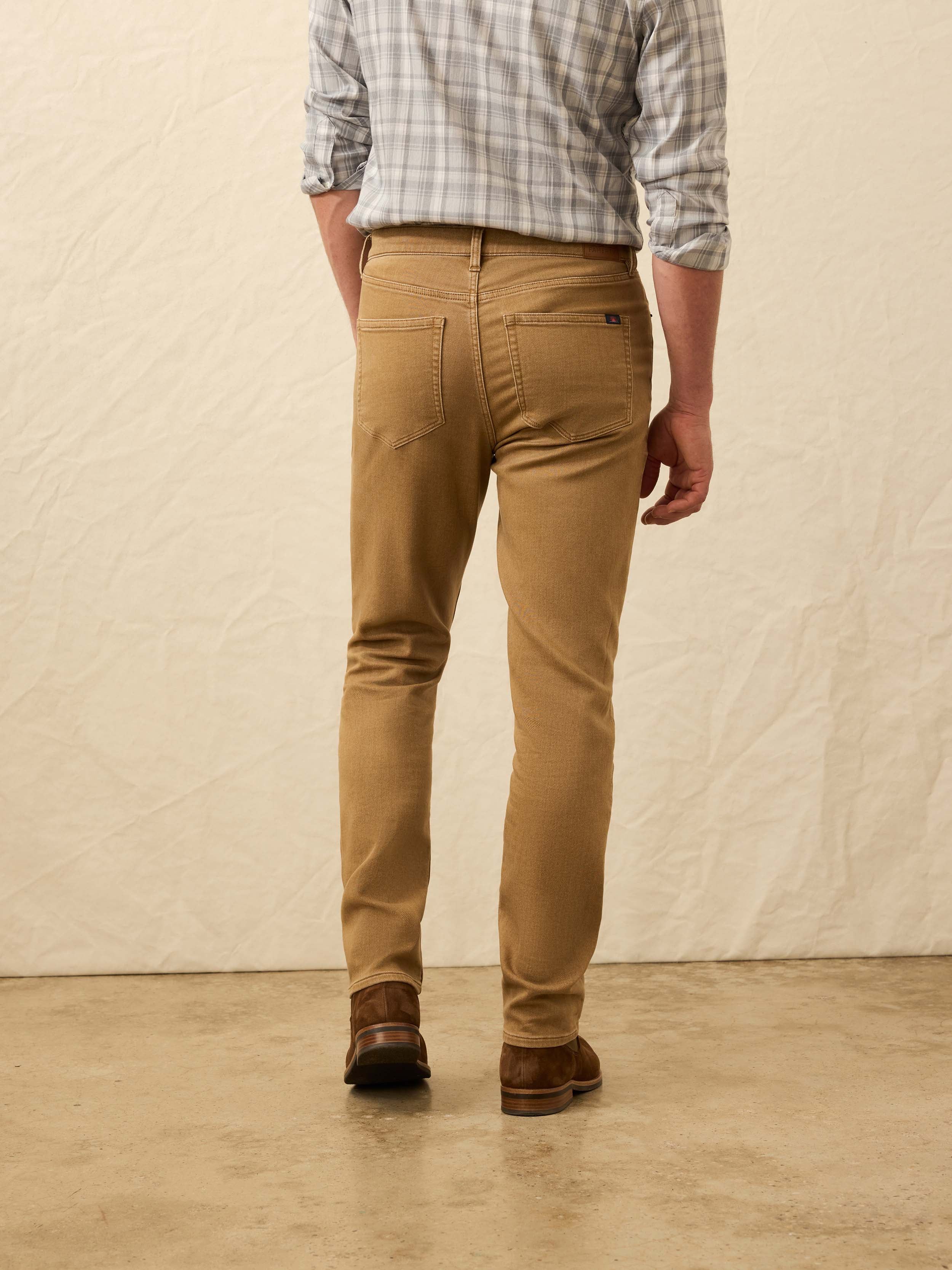 Back view of man wearing a plaid shirt, light brown pants, and brown shoes against a beige background