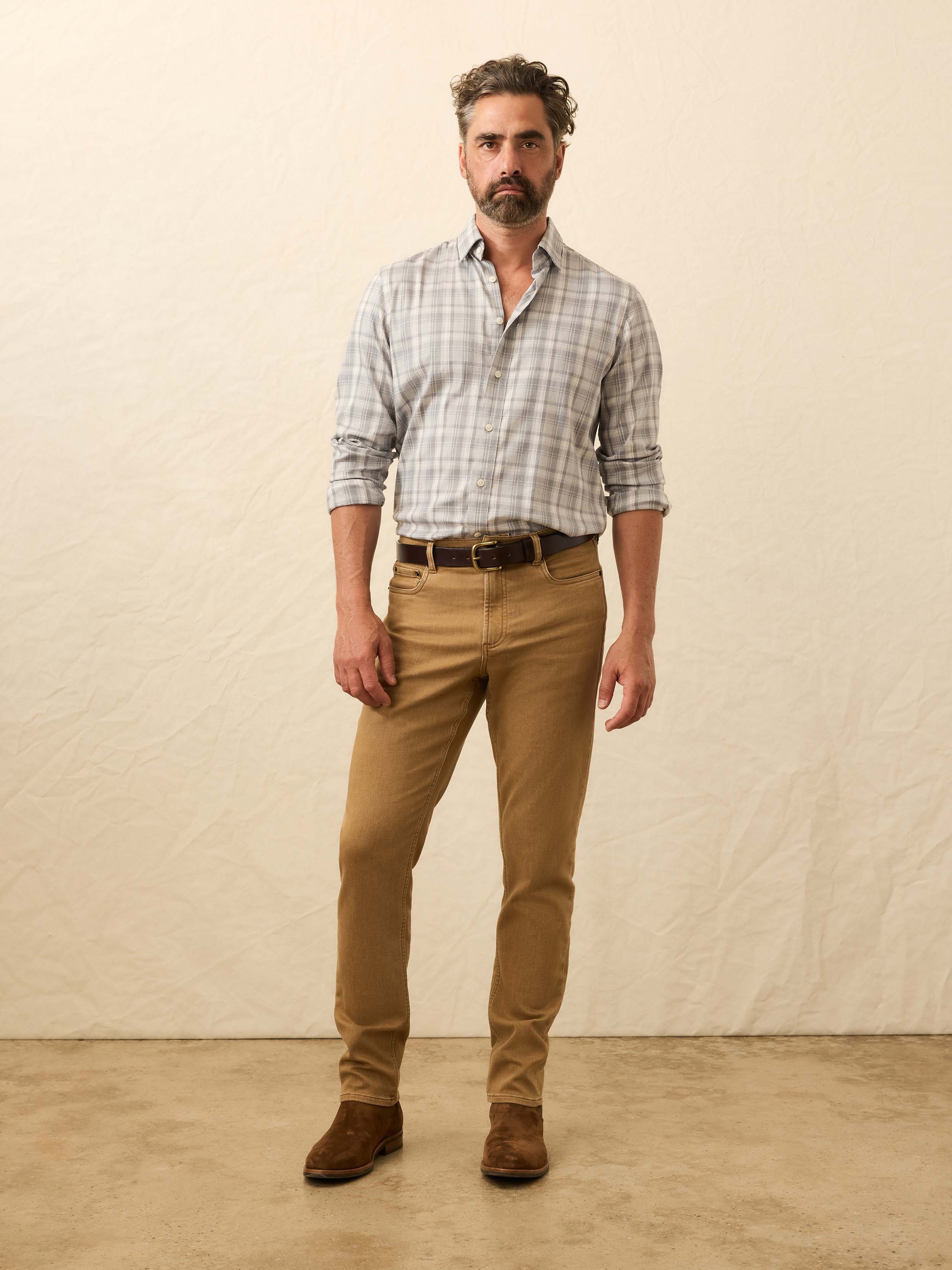 Man wearing a plaid shirt, light brown pants, and brown shoes against a beige background