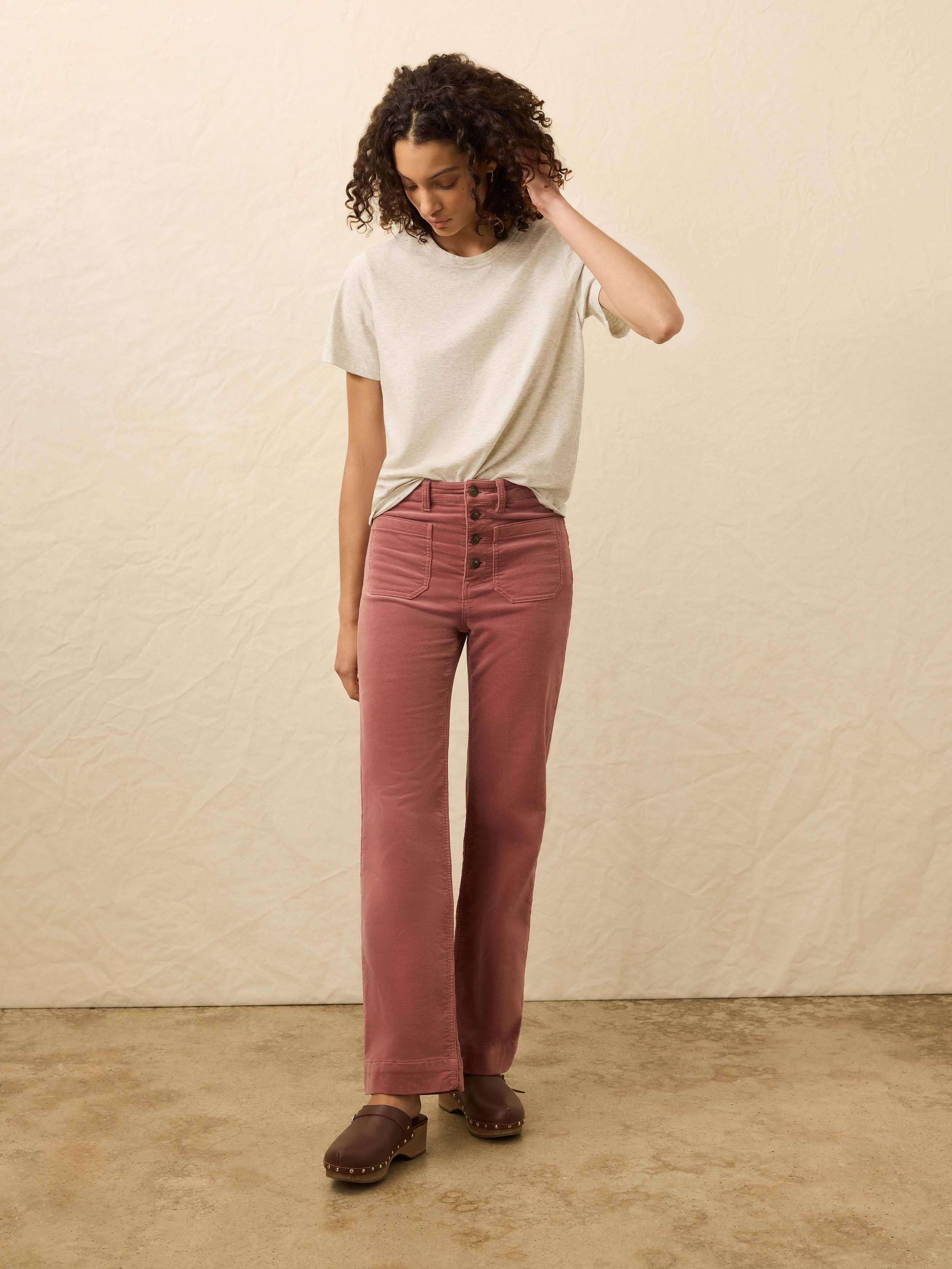 Woman wearing a light heather grey t-shirt and pink corduroy pants against a beige background