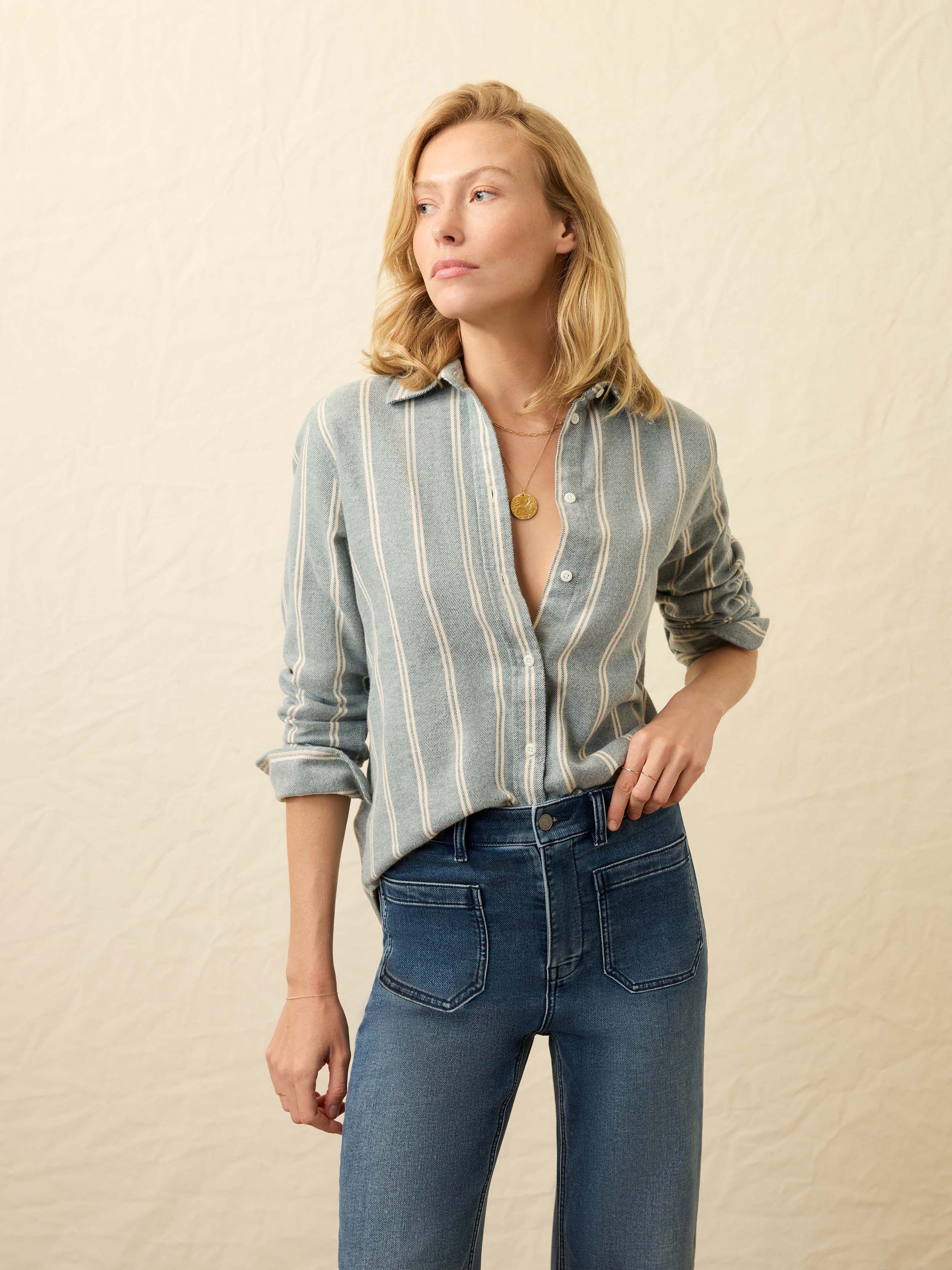 Woman wearing a light blue and white striped denim shirt with blue jeans against a beige background