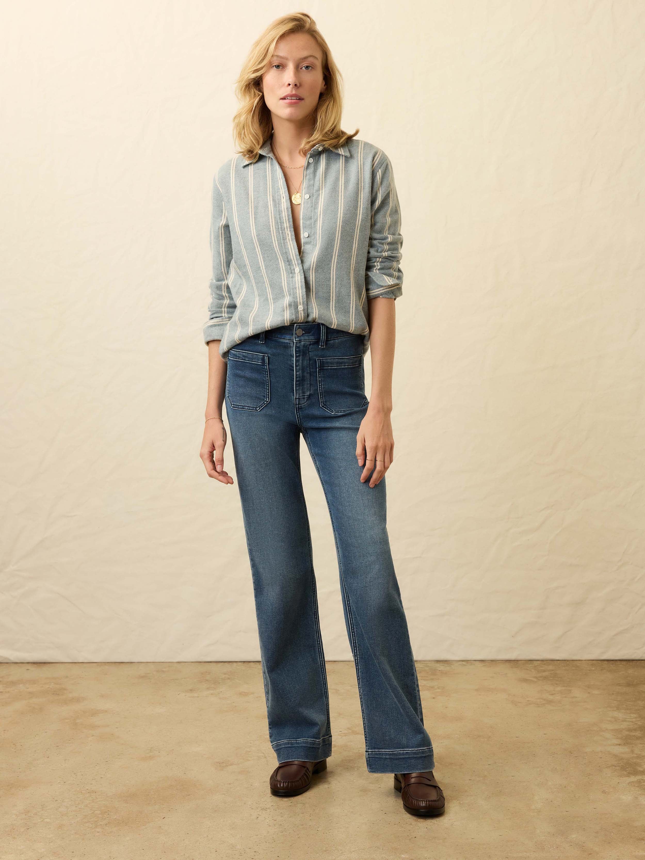 Woman wearing a light blue and white striped denim shirt with blue jeans against a beige background