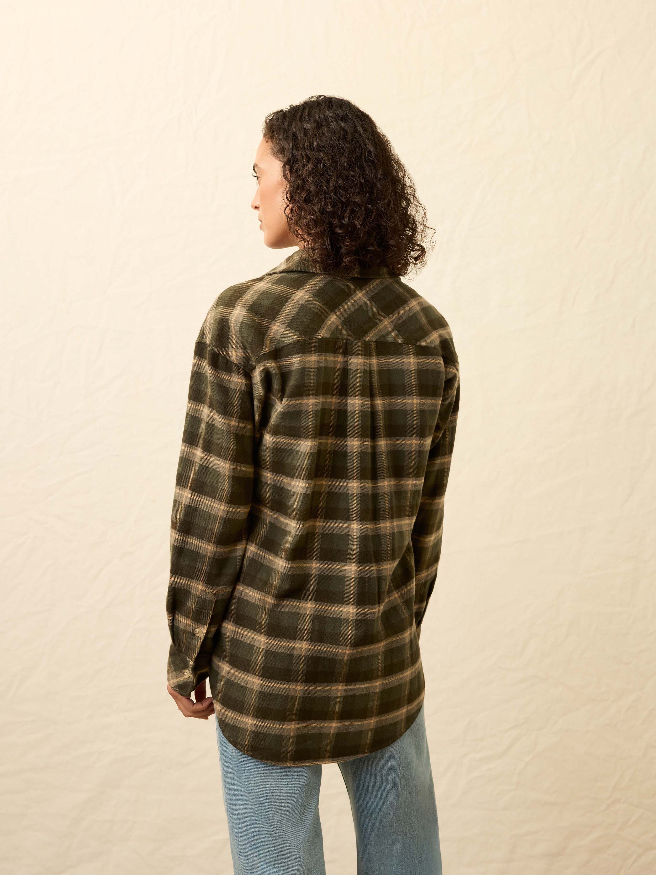 Woman wearing a green plaid shirt and light blue jeans against a beige background