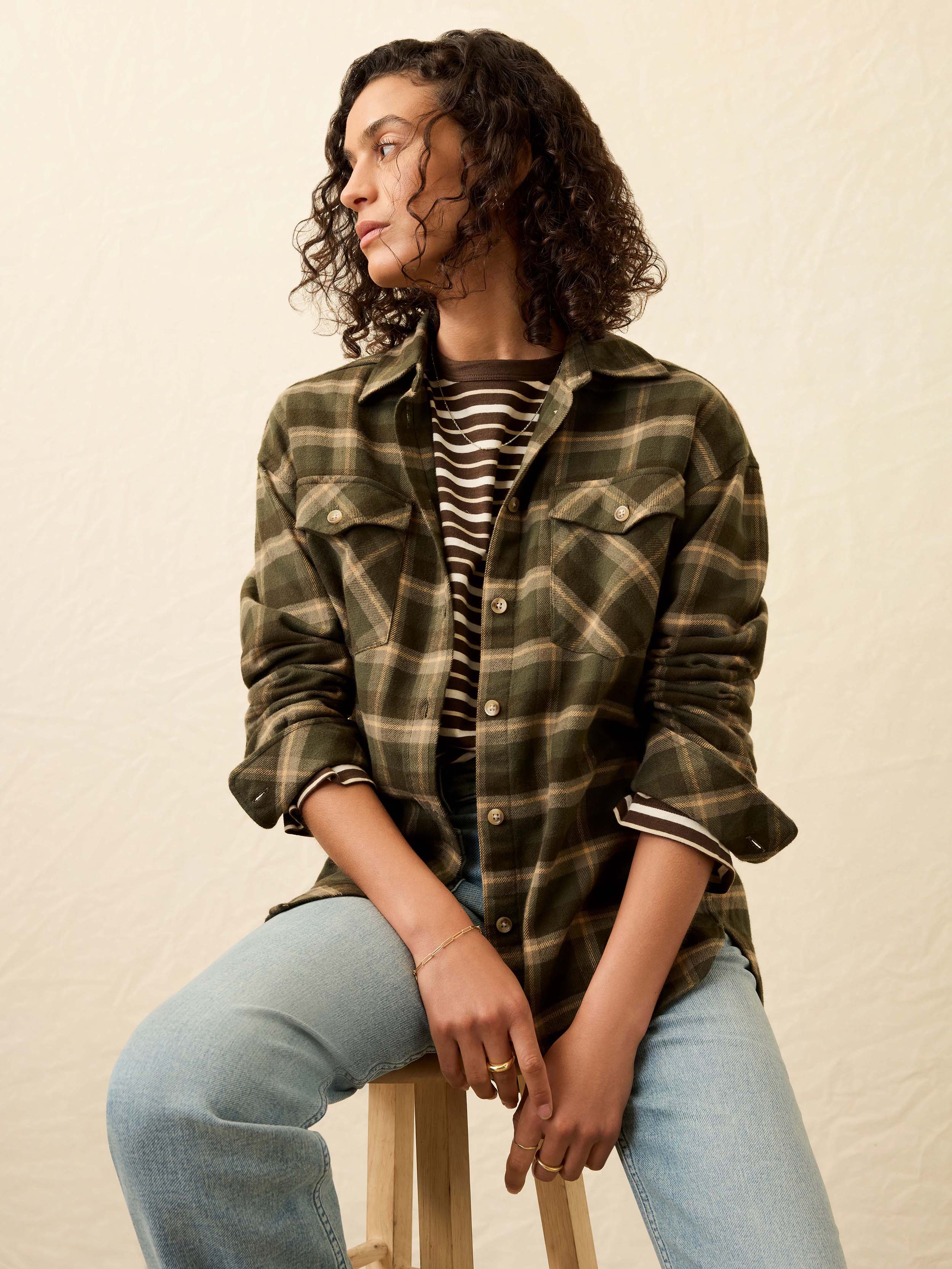 Woman wearing a green plaid shirt and light blue jeans against a beige background