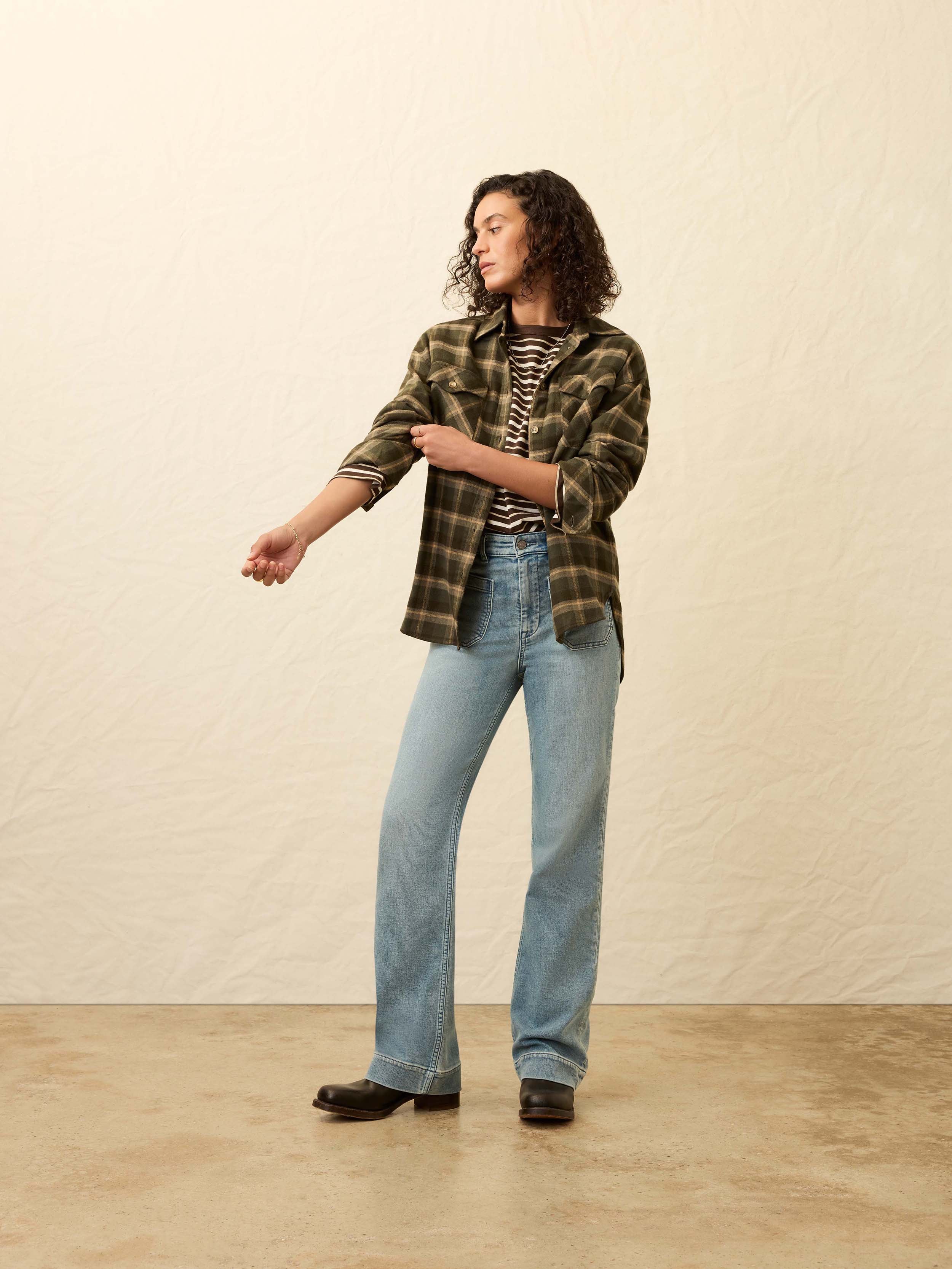 Woman wearing a green plaid shirt and light blue jeans against a beige background