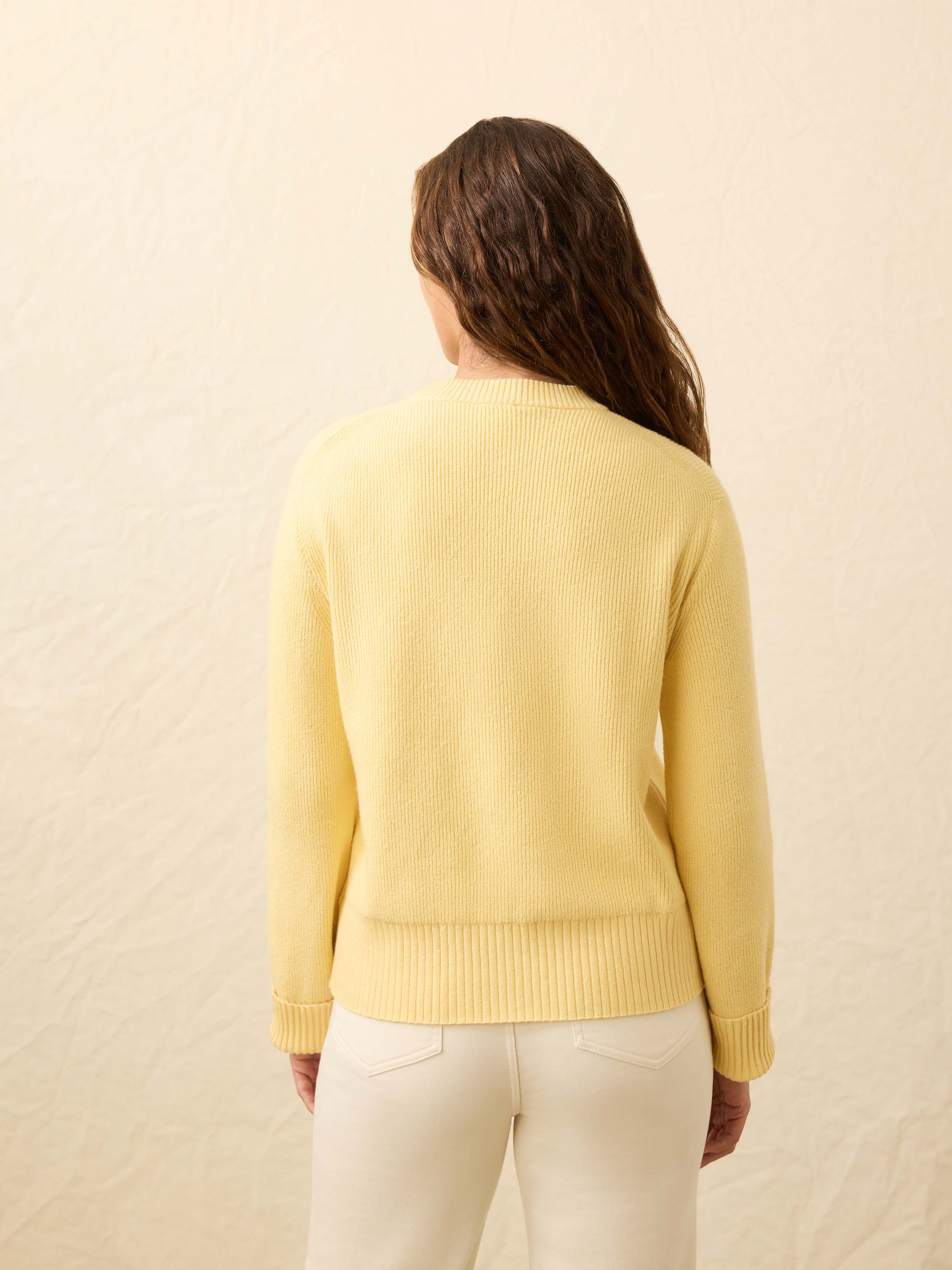 Back view of a woman wearing a yellow sweater with Arizona State University graphic on the left chest against a beige background