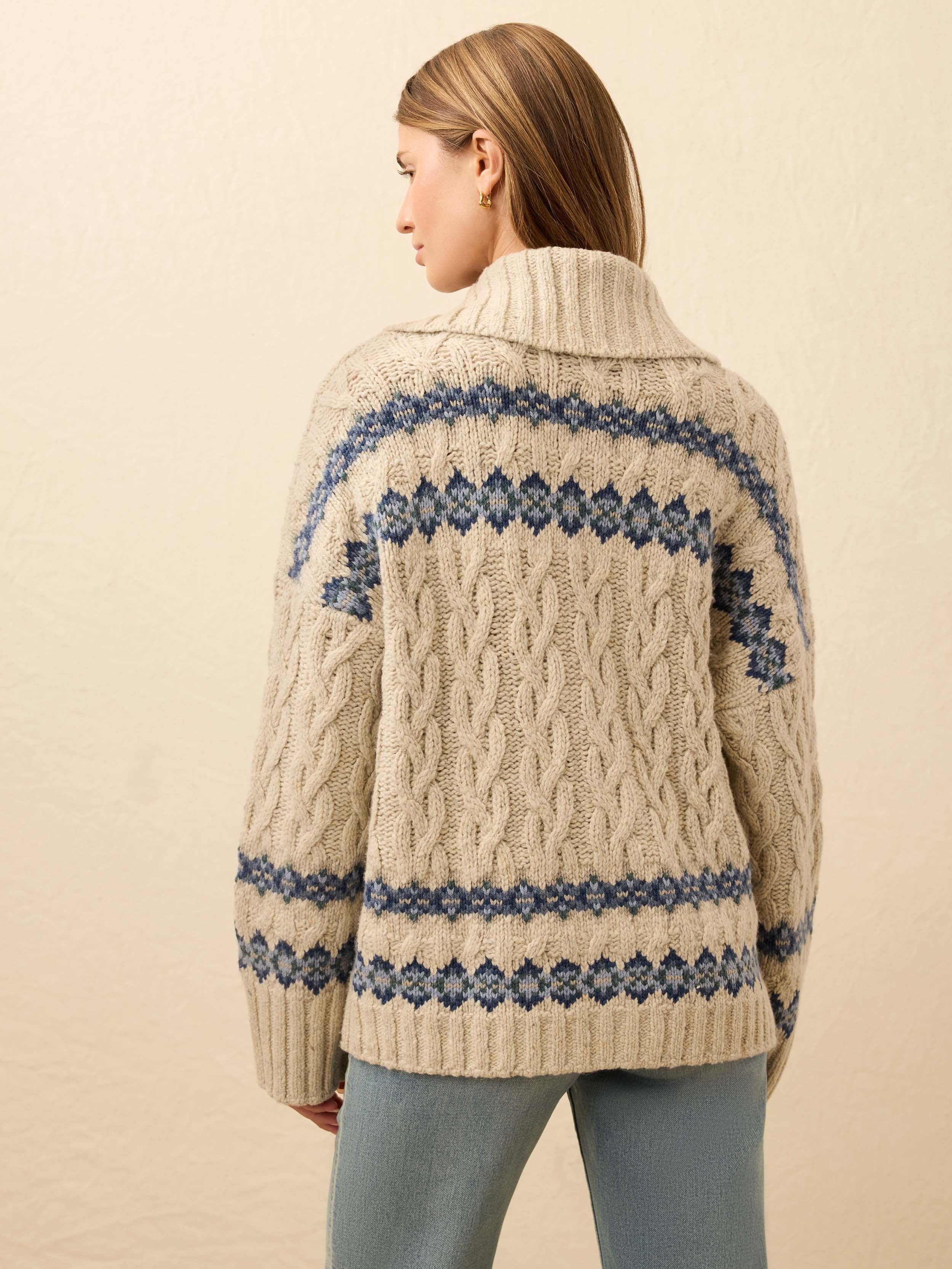 Back view of a woman wearing a cream-colored knit cardigan with blue fairisle pattern on a beige background