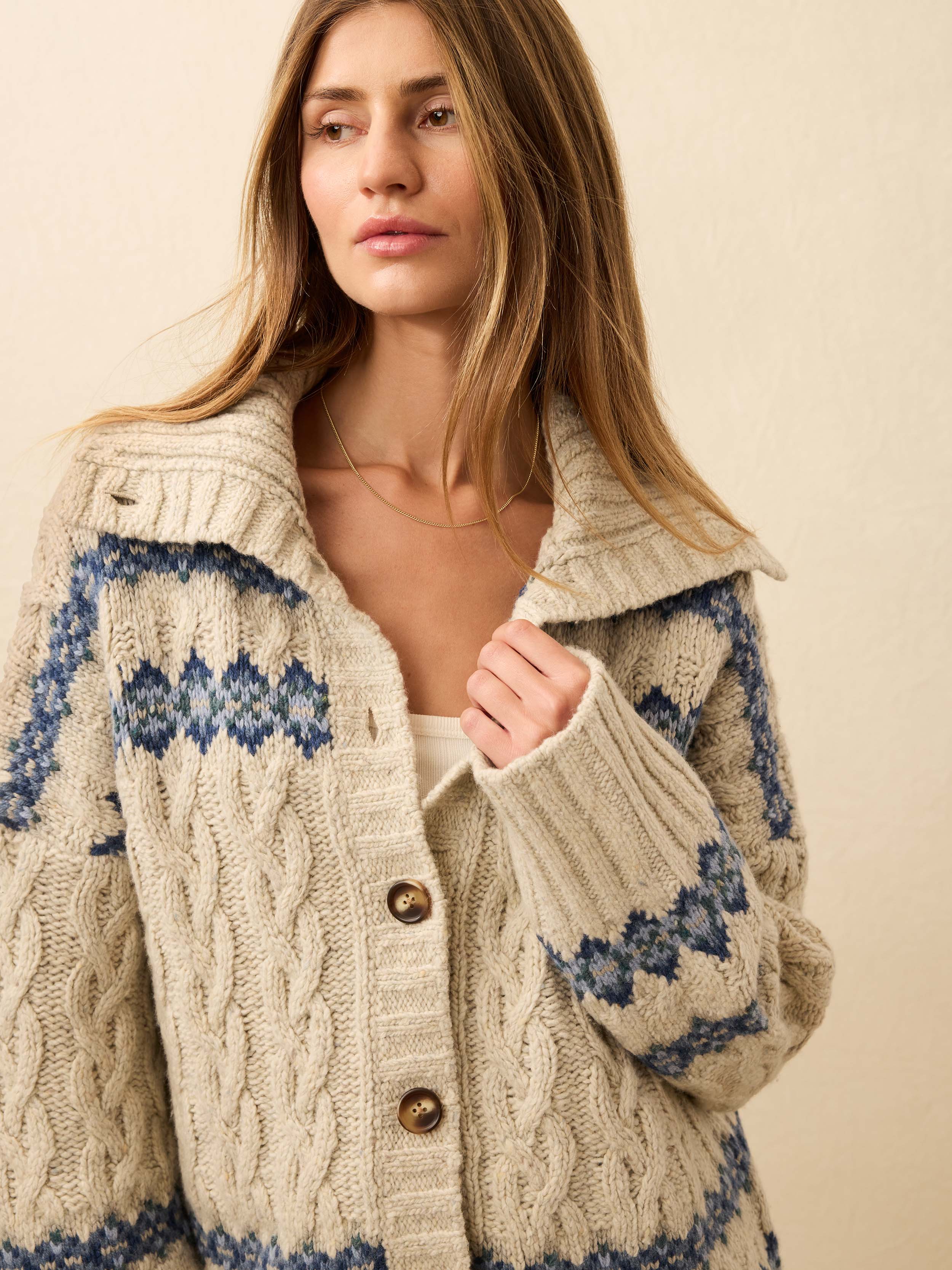 Woman wearing a cream-colored knit cardigan with blue fairisle pattern on a beige background