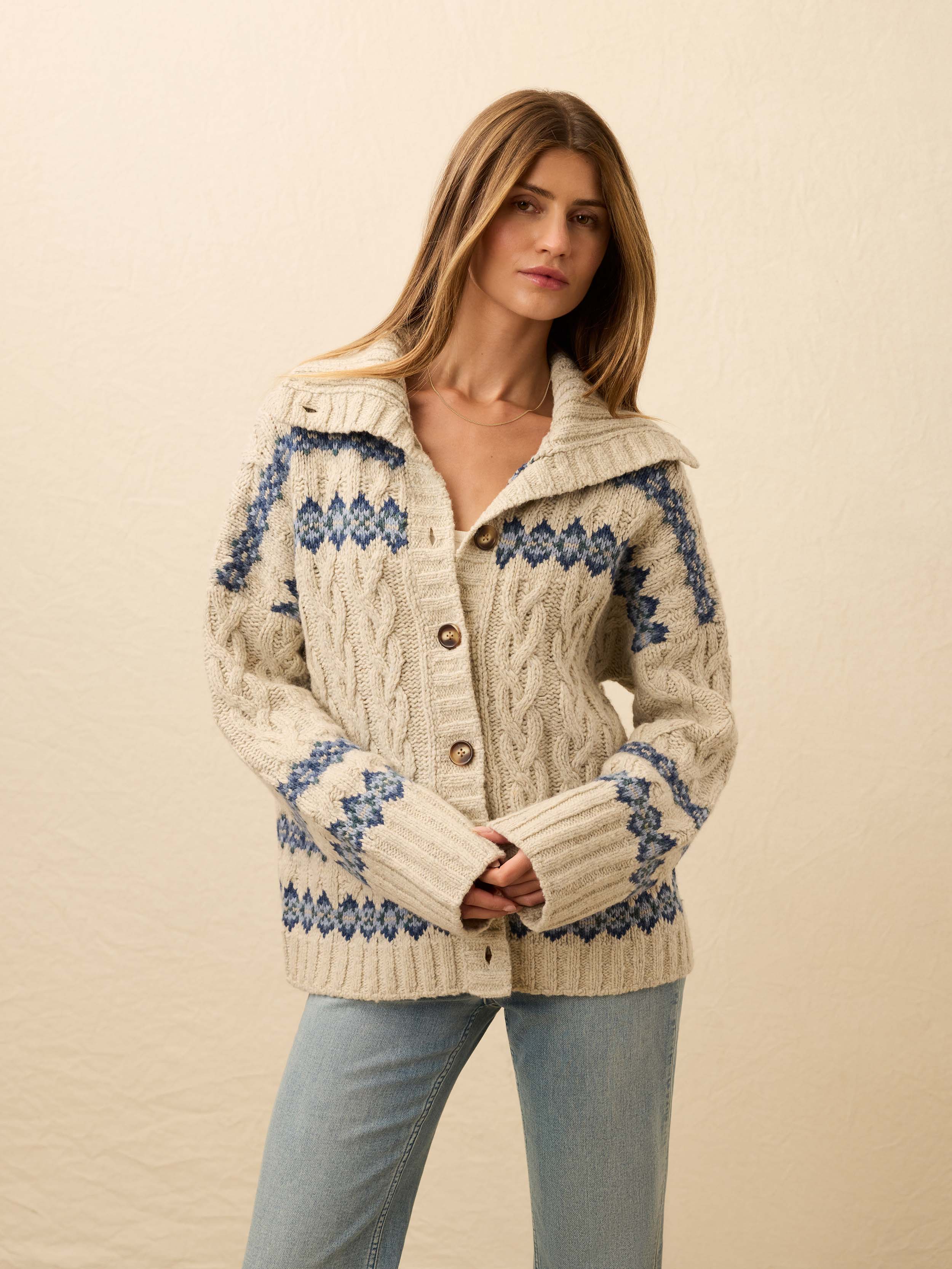Woman wearing a cream-colored knit cardigan with blue fairisle pattern on a beige background