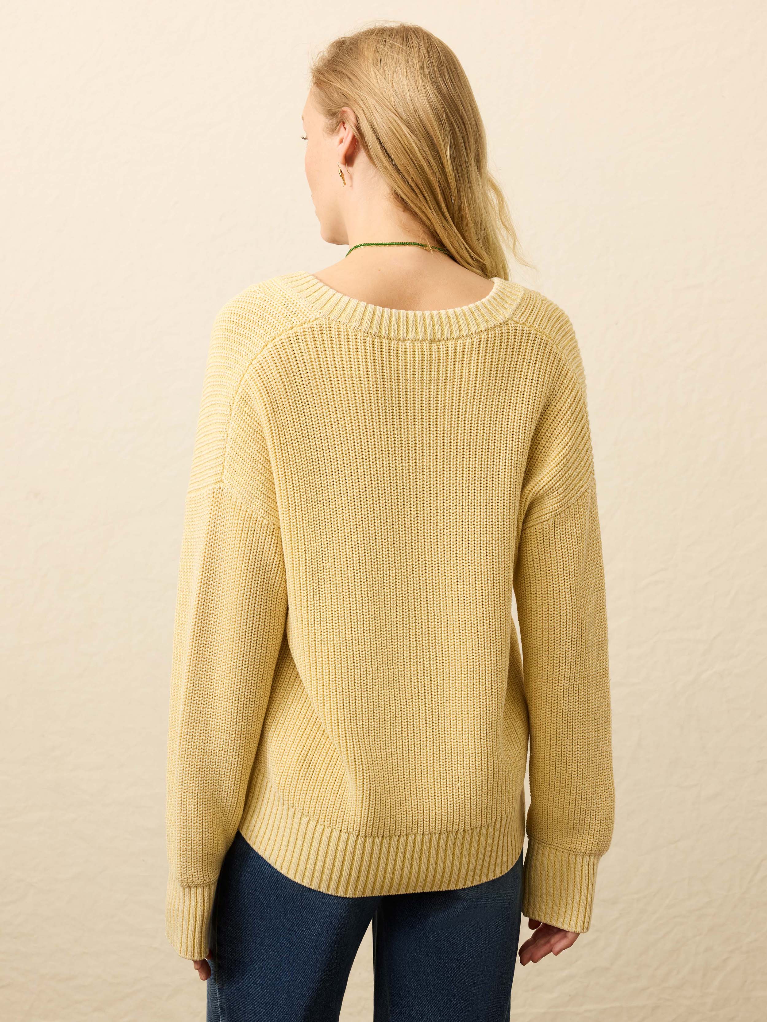 Back view of a woman wearing a yellow ribbed sweater with Arizona State University graphic against a beige background