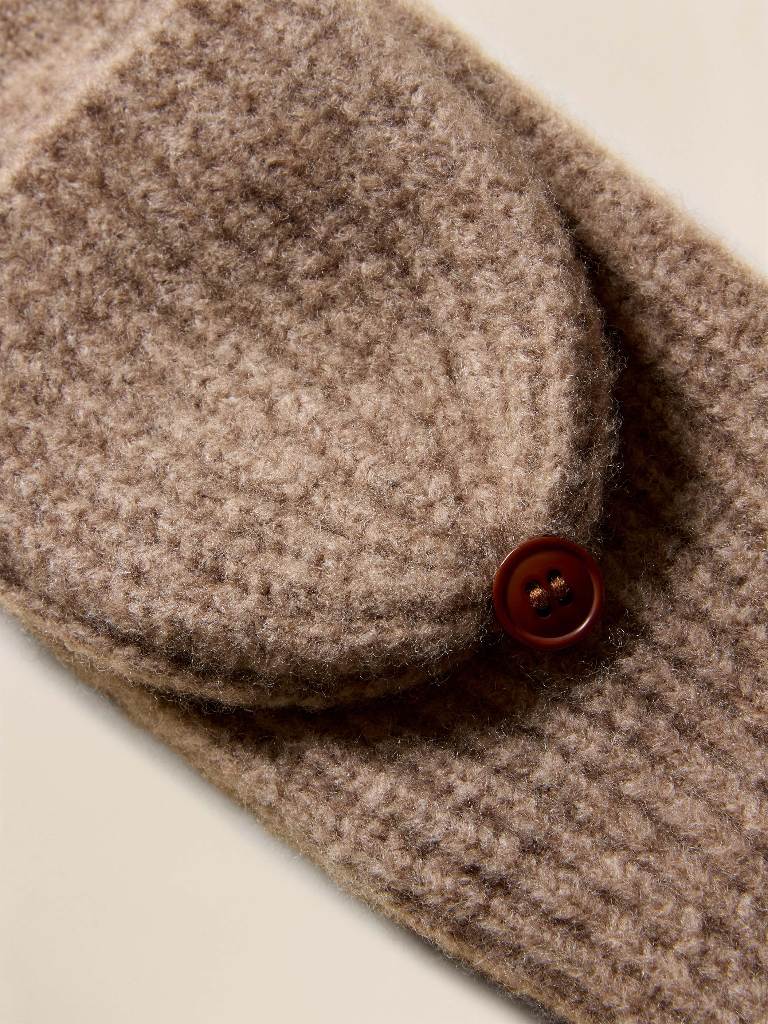 Close-up of a brown knitted gloves with a button on a beige background