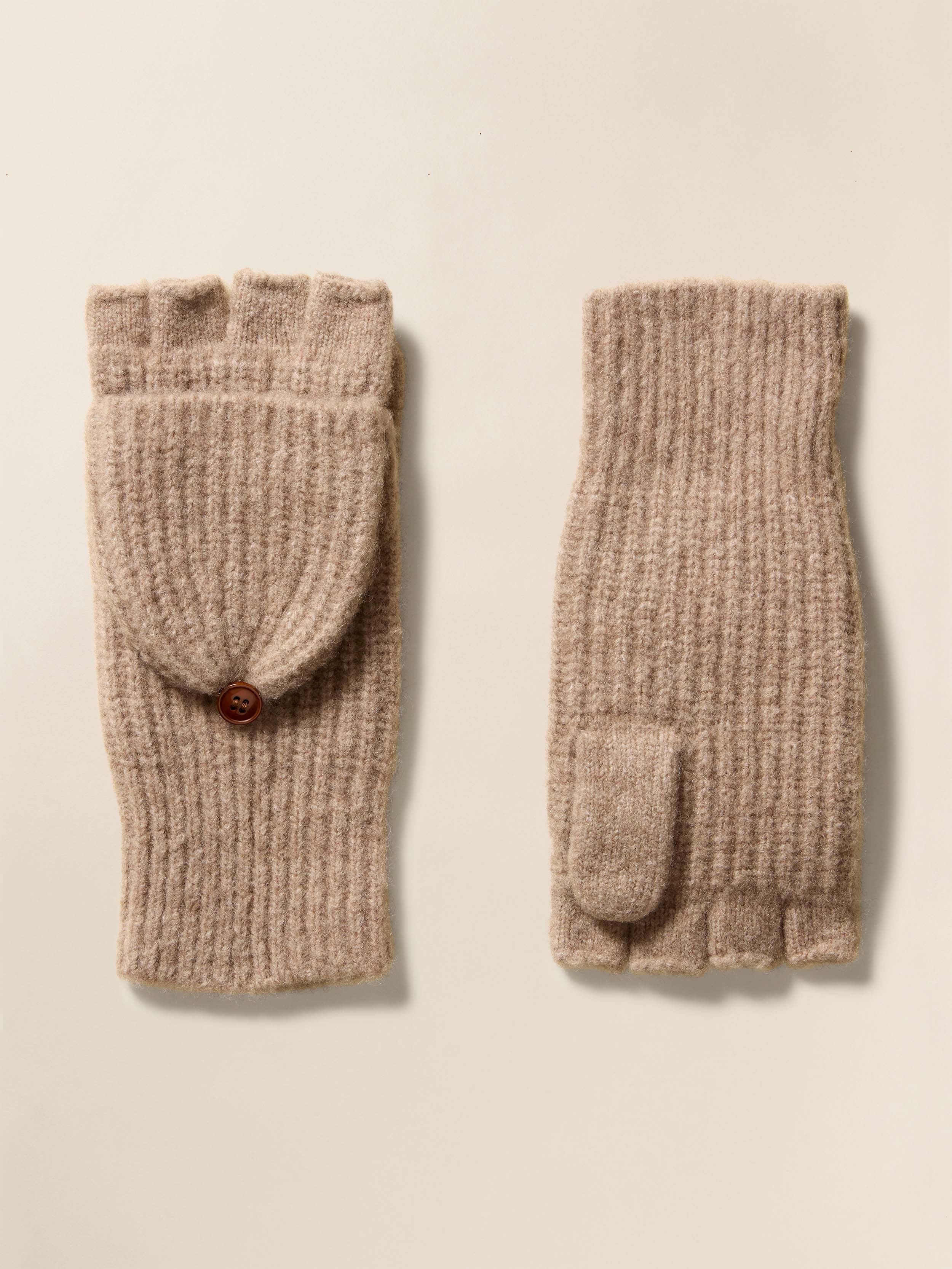 Pair of beige knitted fingerless gloves with a button on a beige background