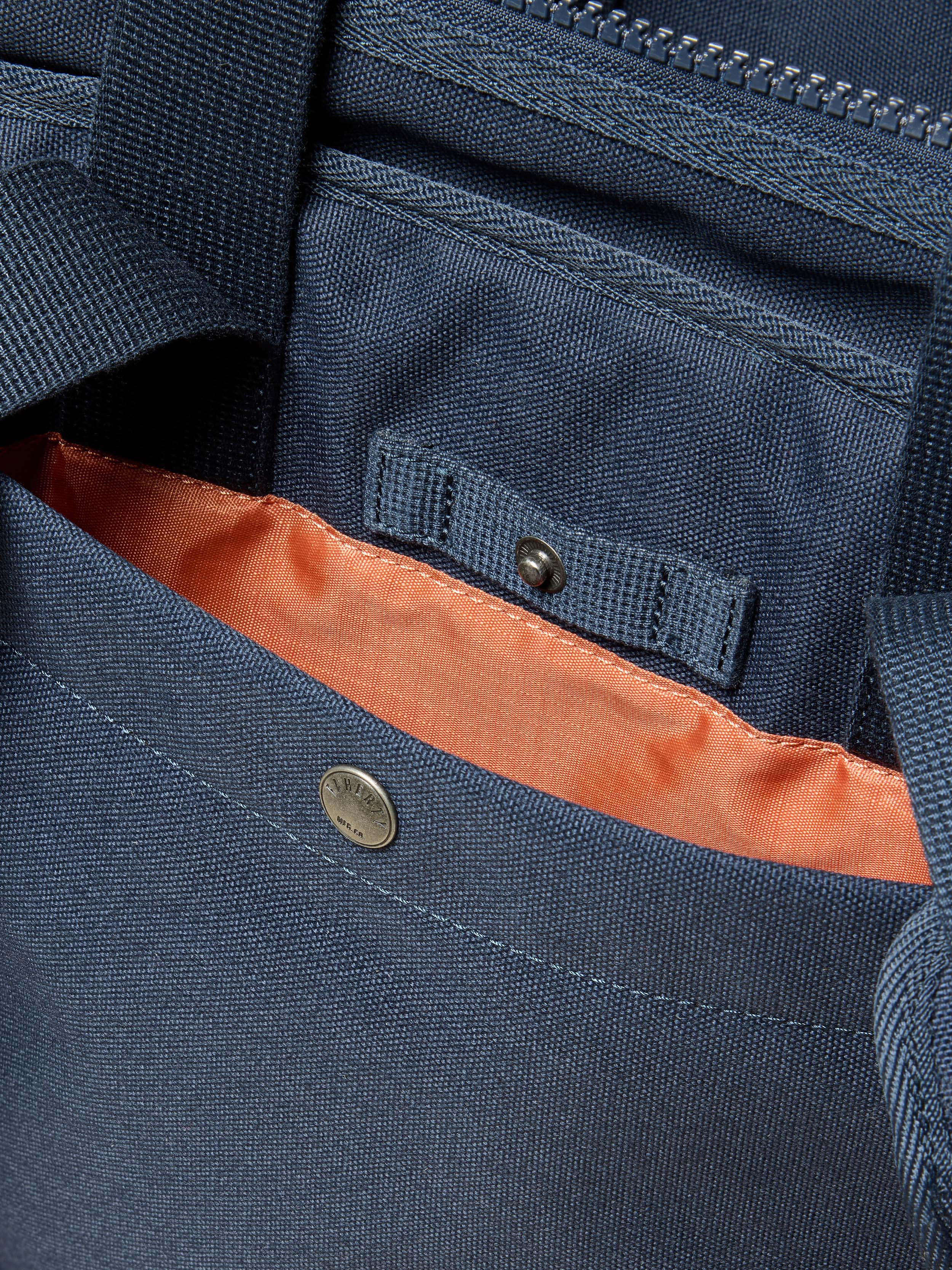 Close-up of a blue backpack with an orange interior lining, featuring a button and zipper.