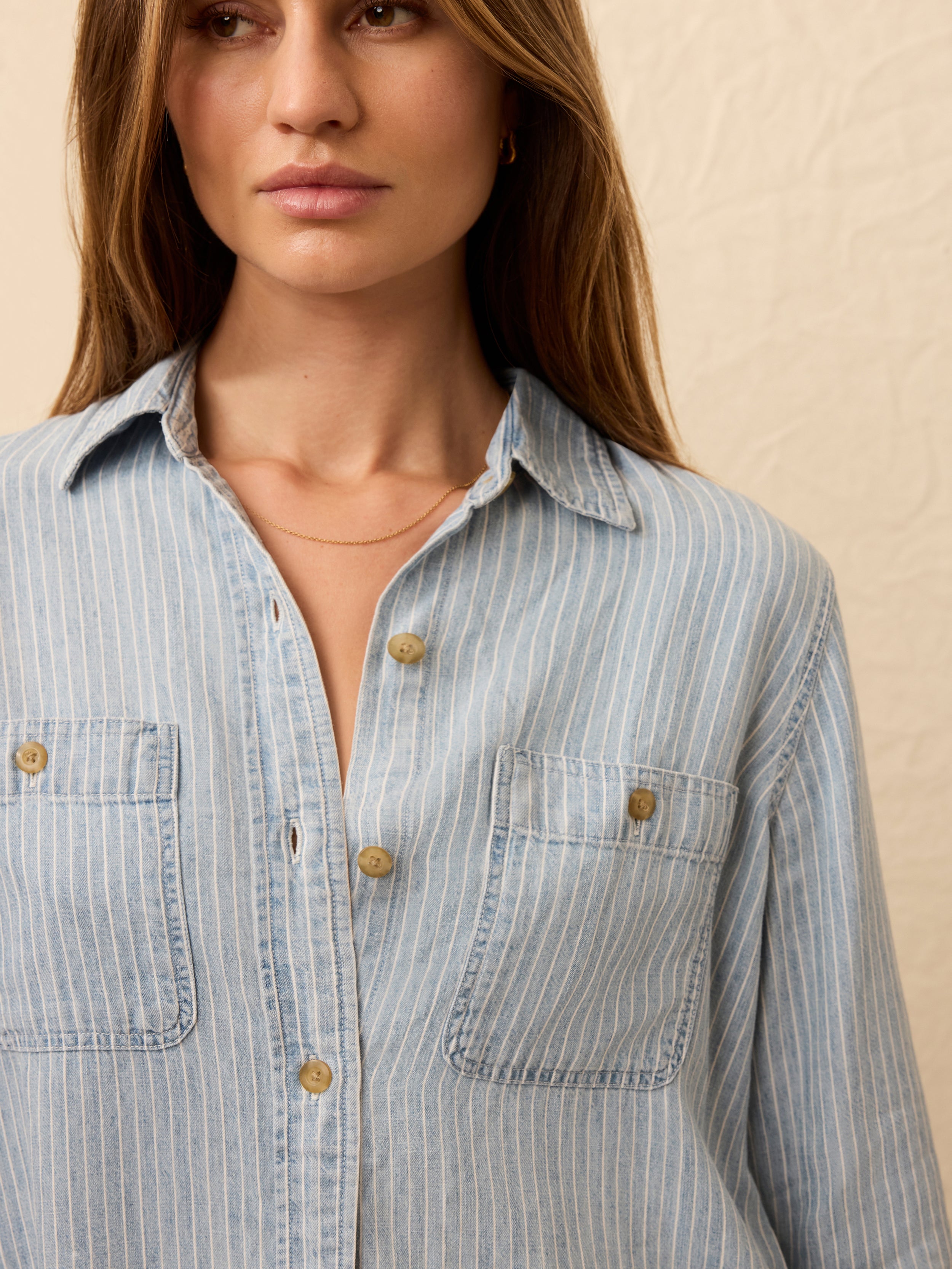 Woman wearing a light blue striped chambray shirt against a beige background