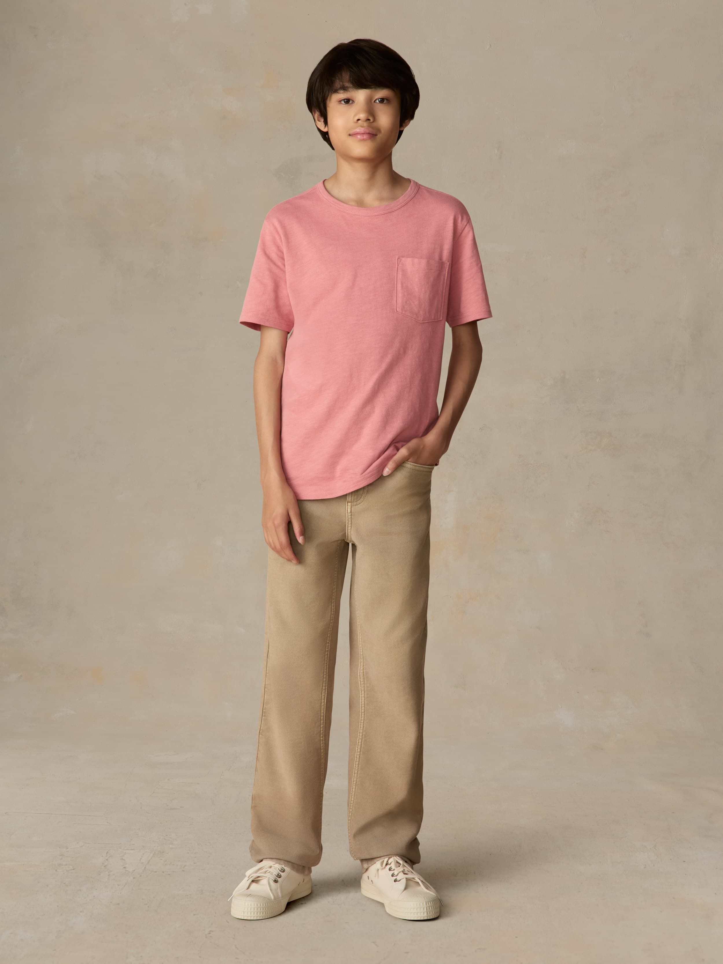 Child wearing a red pocket tee and beige pants against a beige background