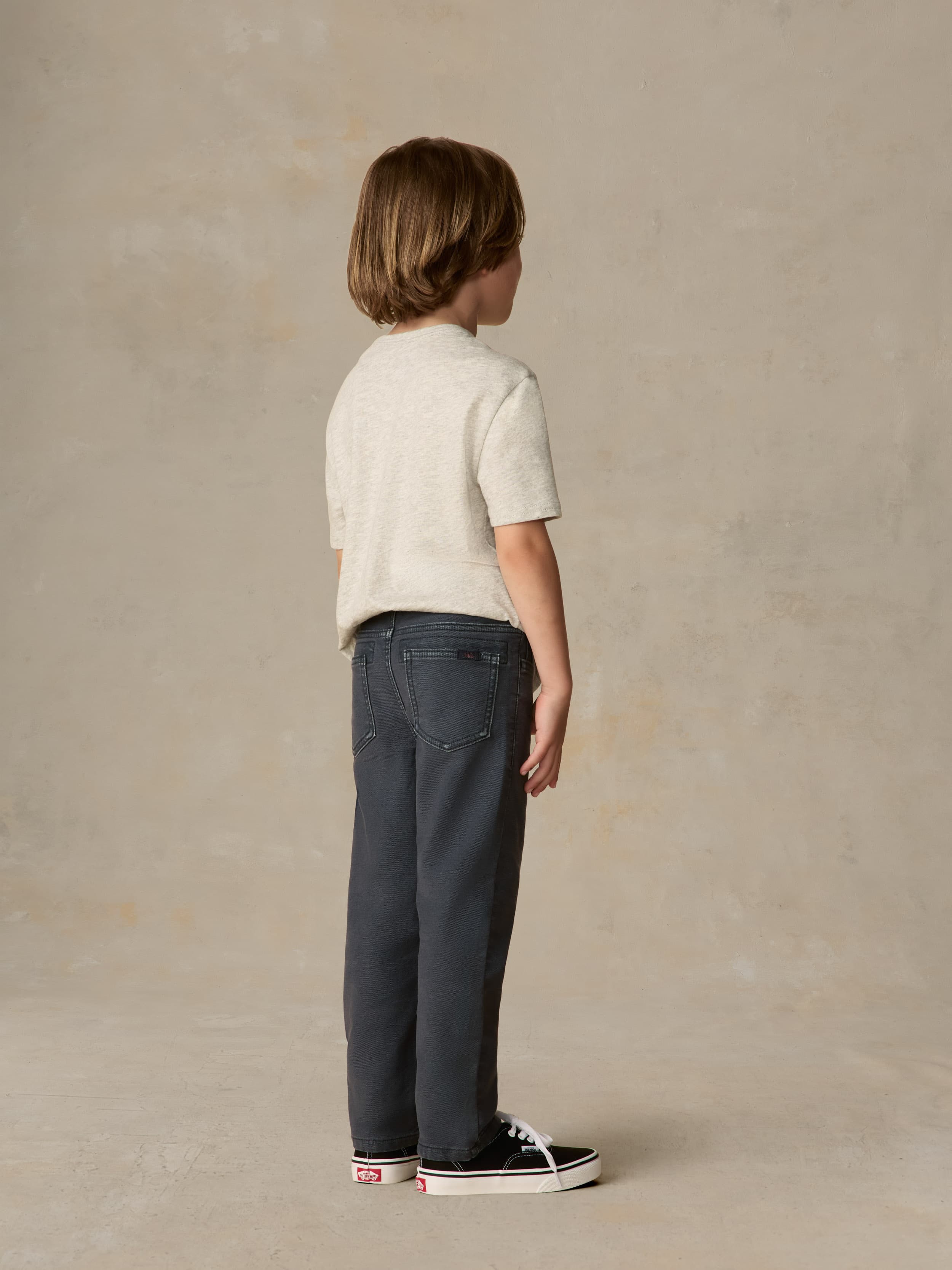 Child wearing a grey surf & ski club tee and black pants against a beige background