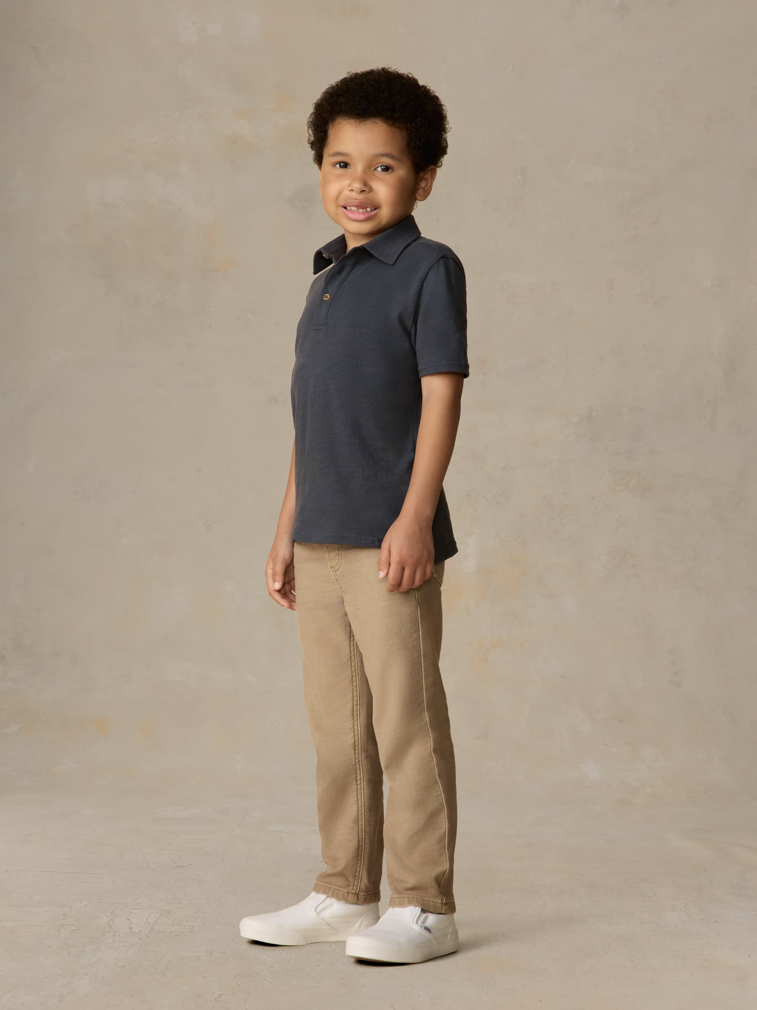 Child wearing a blue polo shirt and beige pants against a beige background