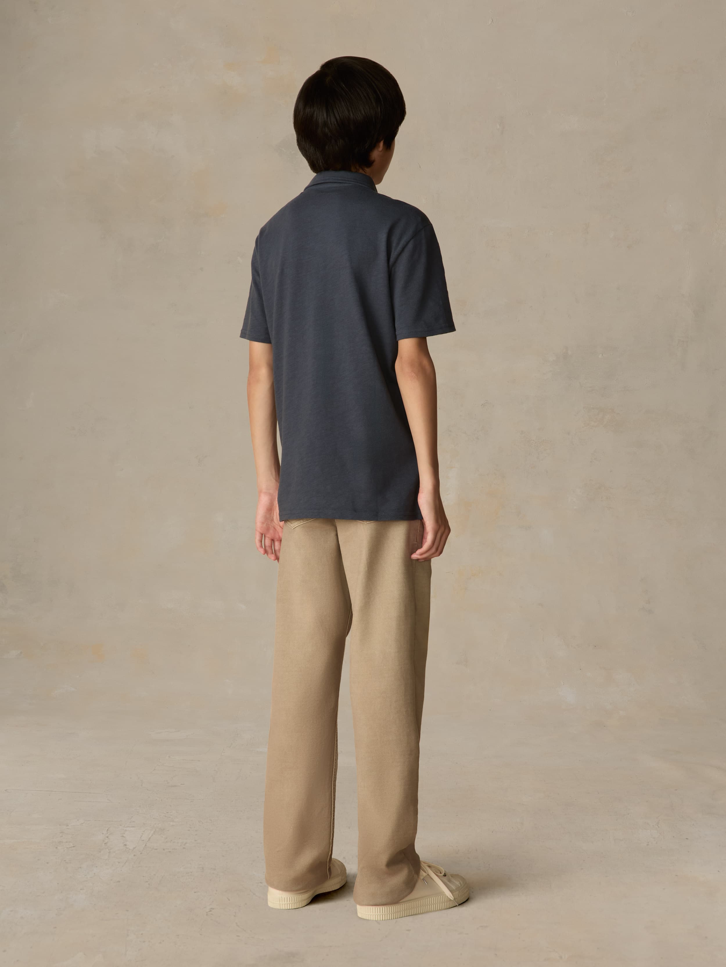 Child wearing a blue polo shirt and beige pants against a beige background