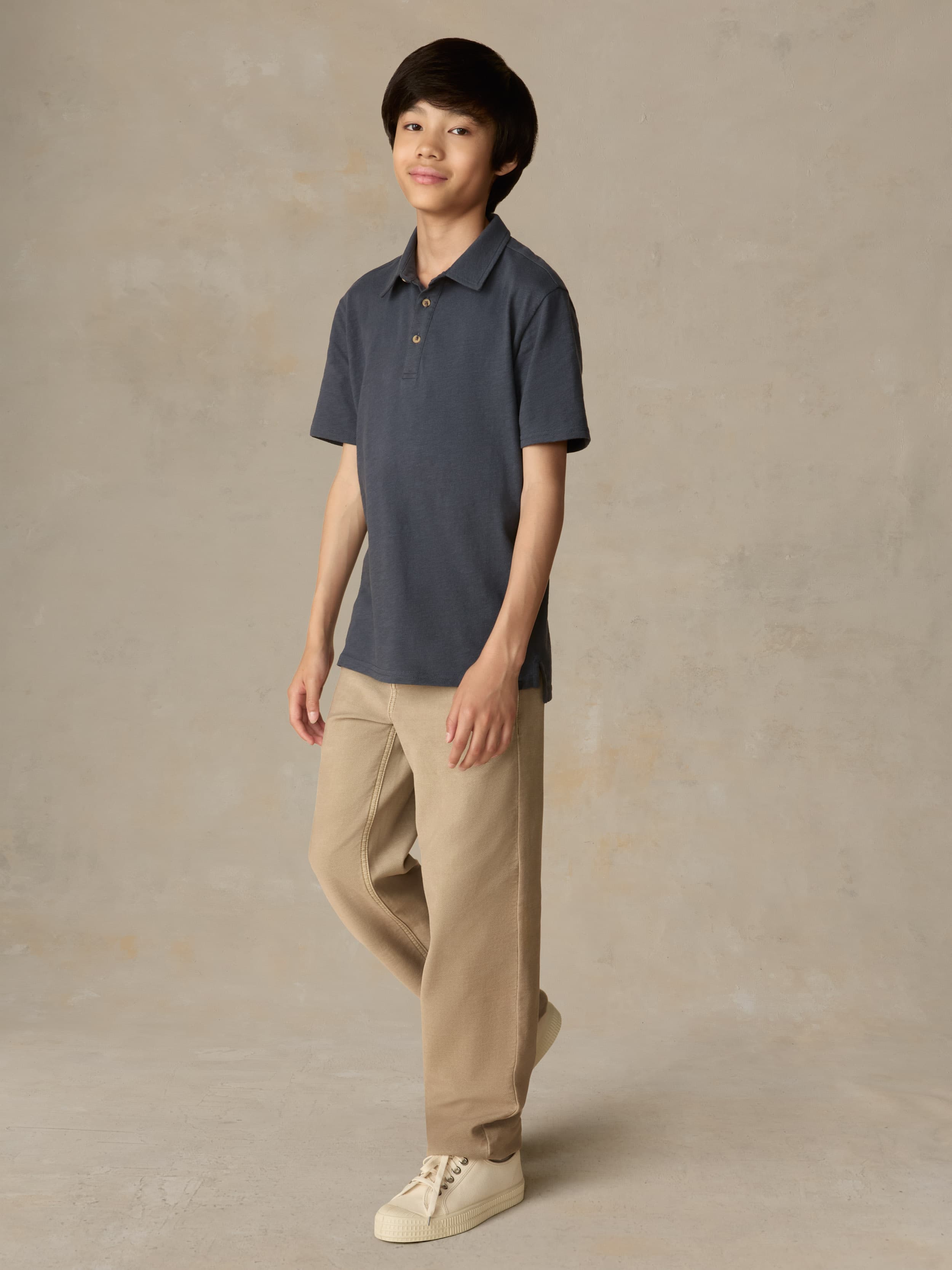 Child wearing a blue polo shirt and beige pants against a beige background