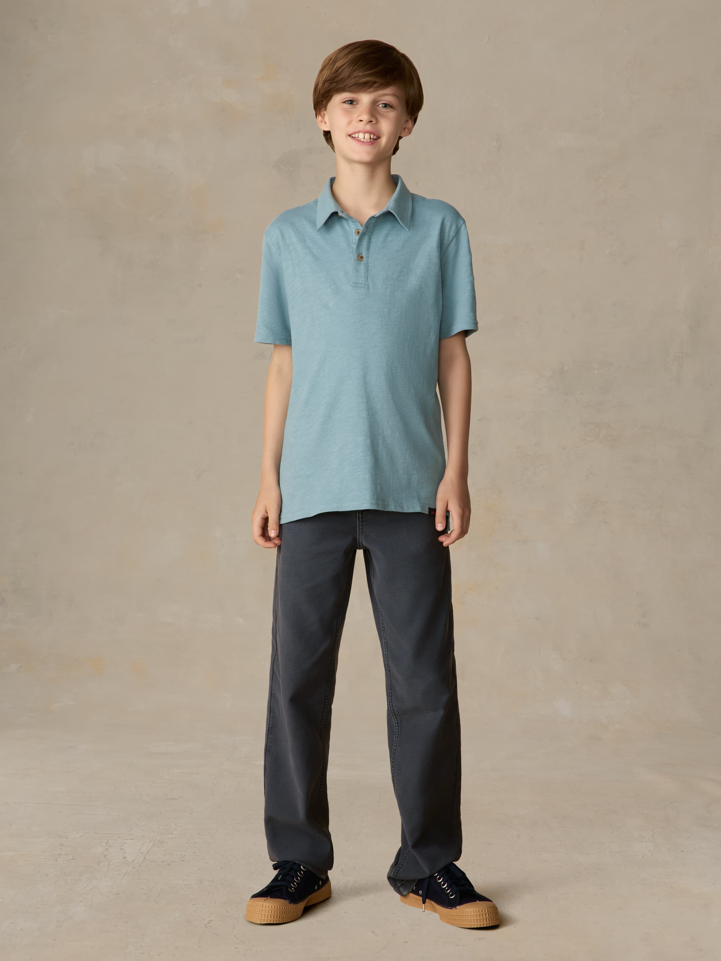 Child wearing a light blue polo and navy pants against a beige background