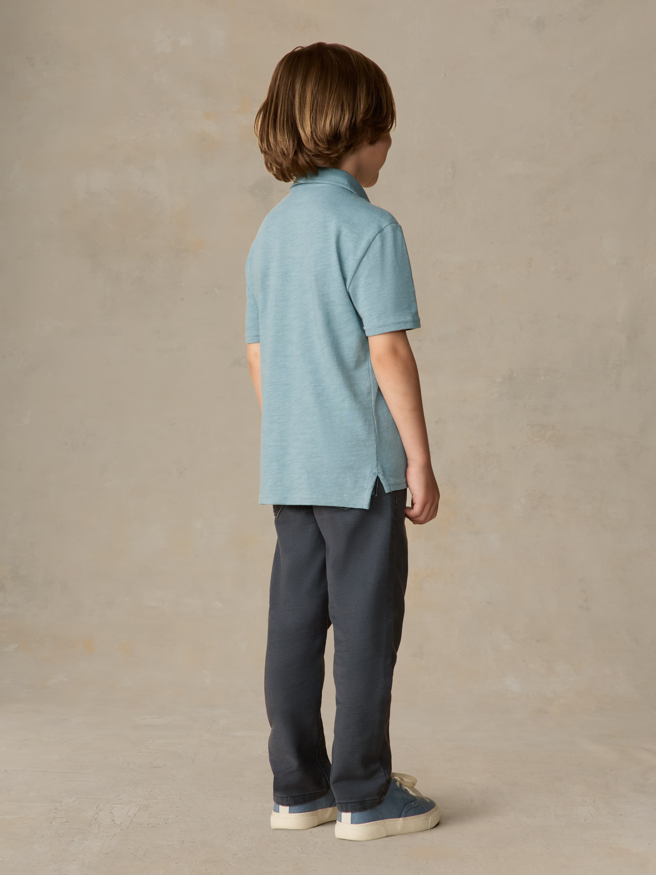 Child wearing a light blue polo shirt and navy pants against a beige background