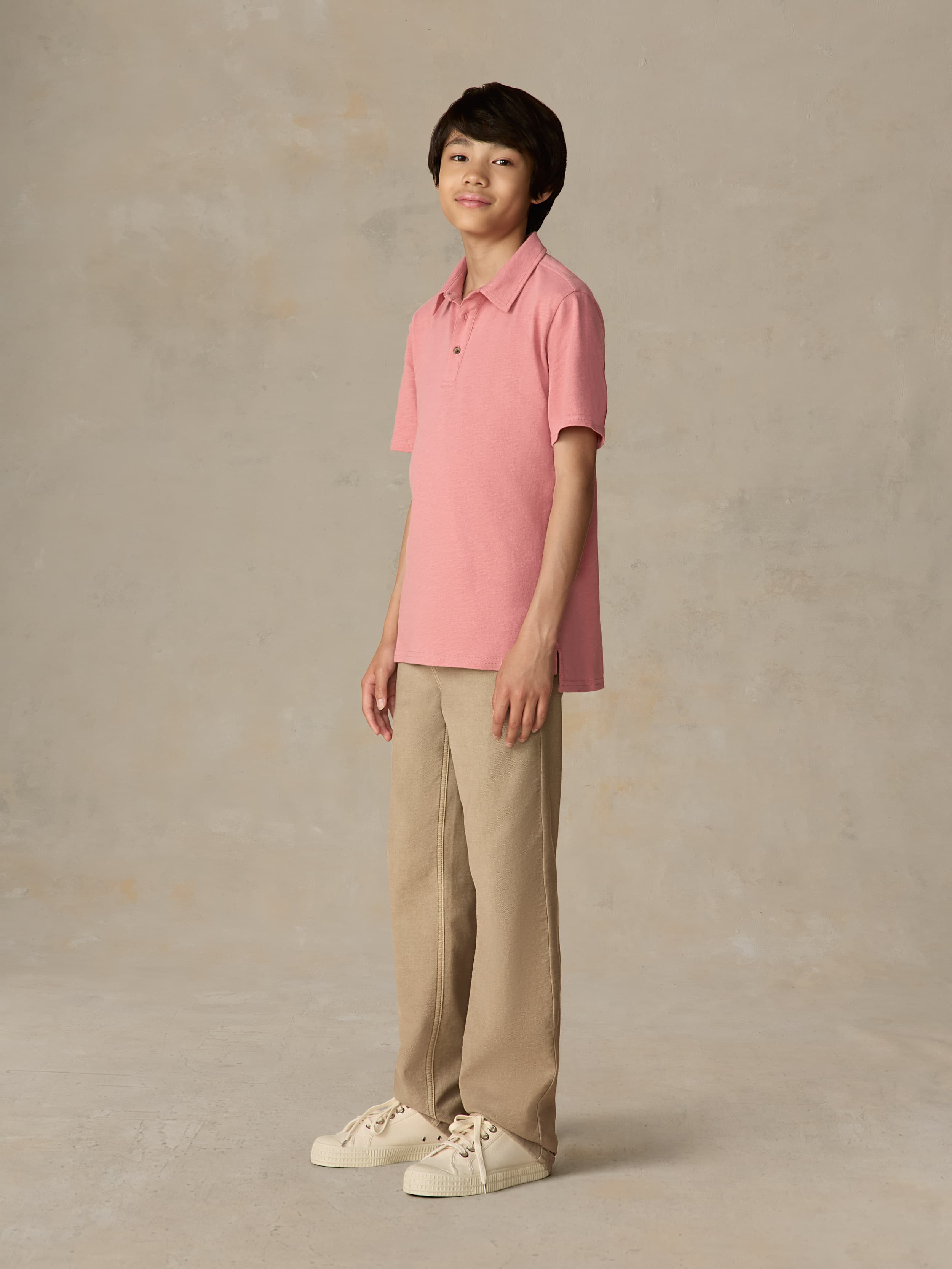 Child wearing a red polo shirt and beige pants against a beige background