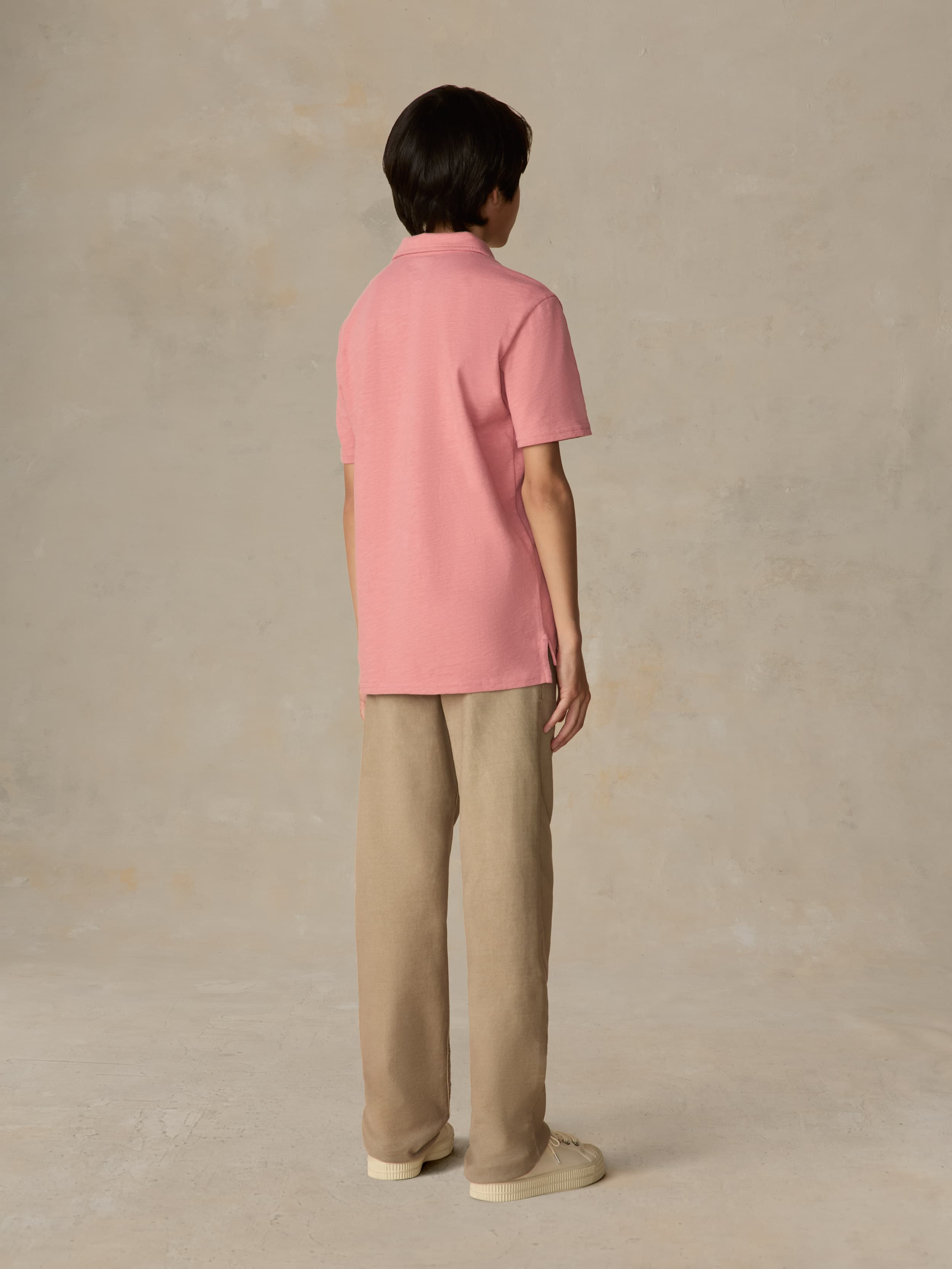 Child wearing a red polo shirt and beige pants against a beige background