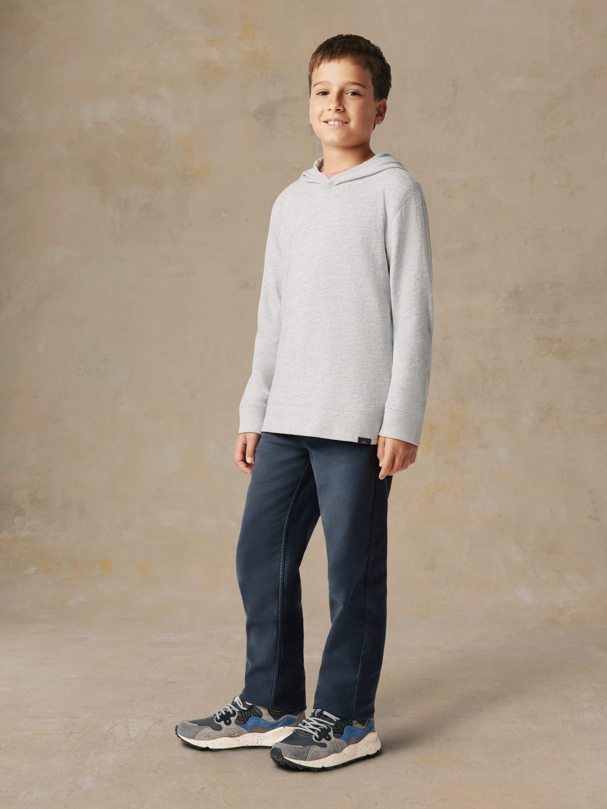 A boy wearing a grey hoodie and blue pants, image 2 of 5