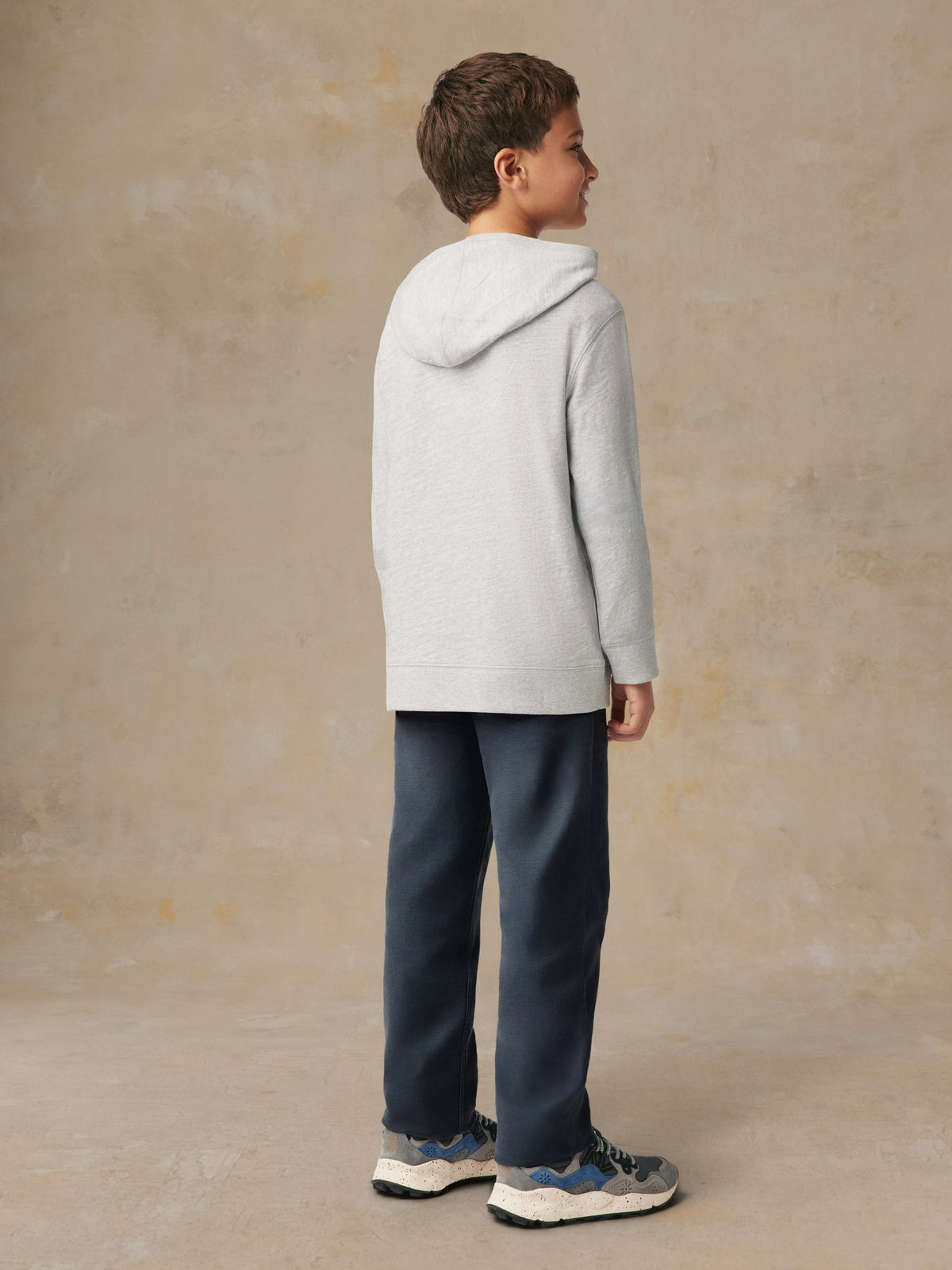 A boy viewed from behind wearing a grey hoodie and blue pants, image 3 of 5