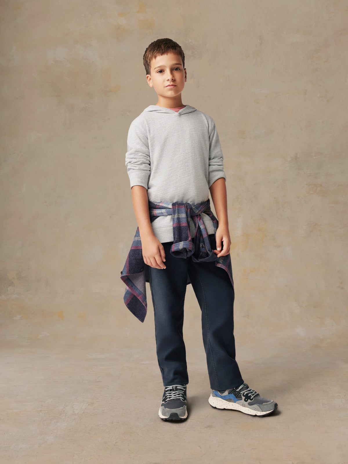 A boy wearing a grey hoodie, flannel shirt, and blue pants, image 5 of 5