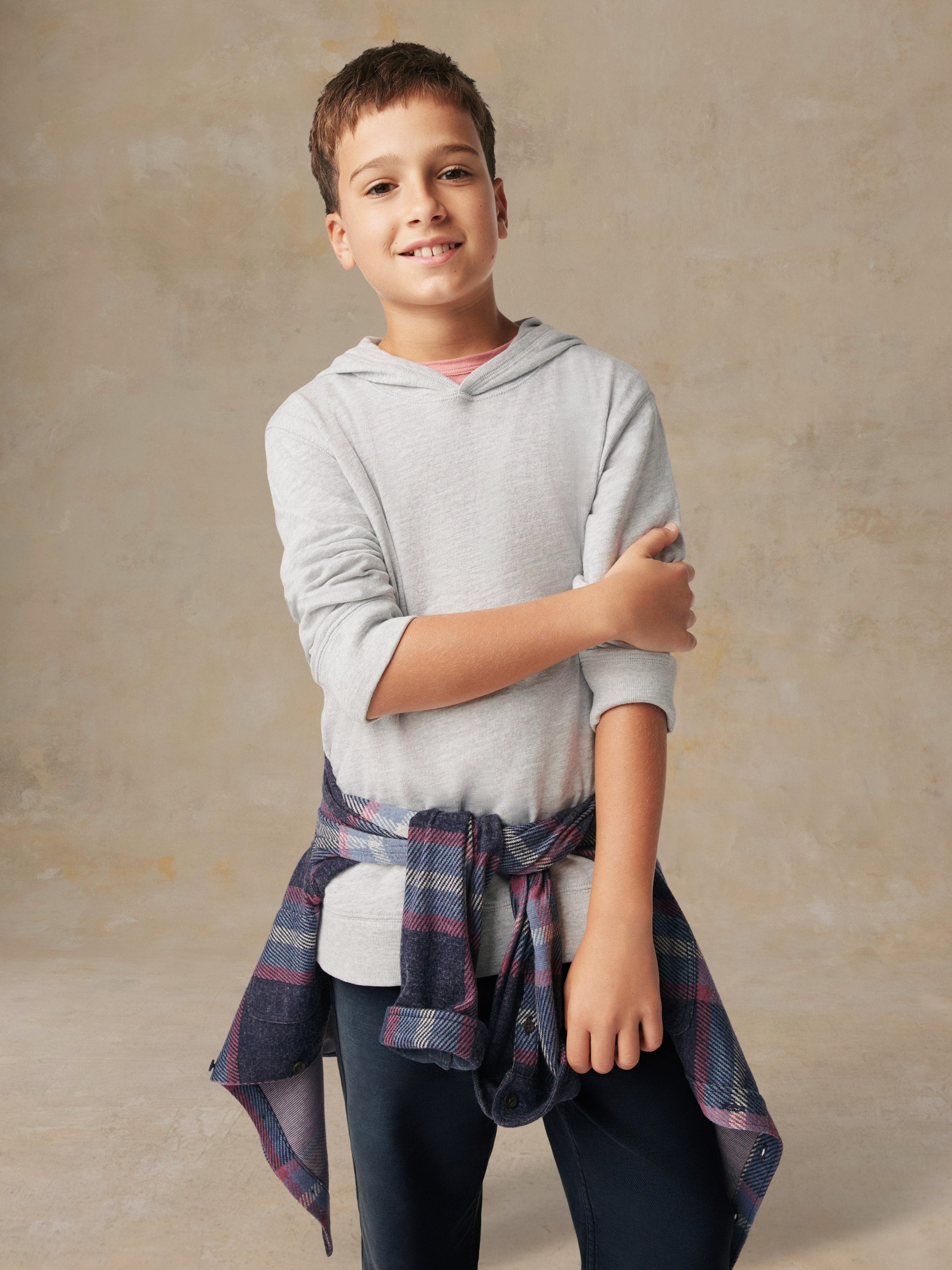 A boy wearing a grey hoodie, flannel, and blue pants