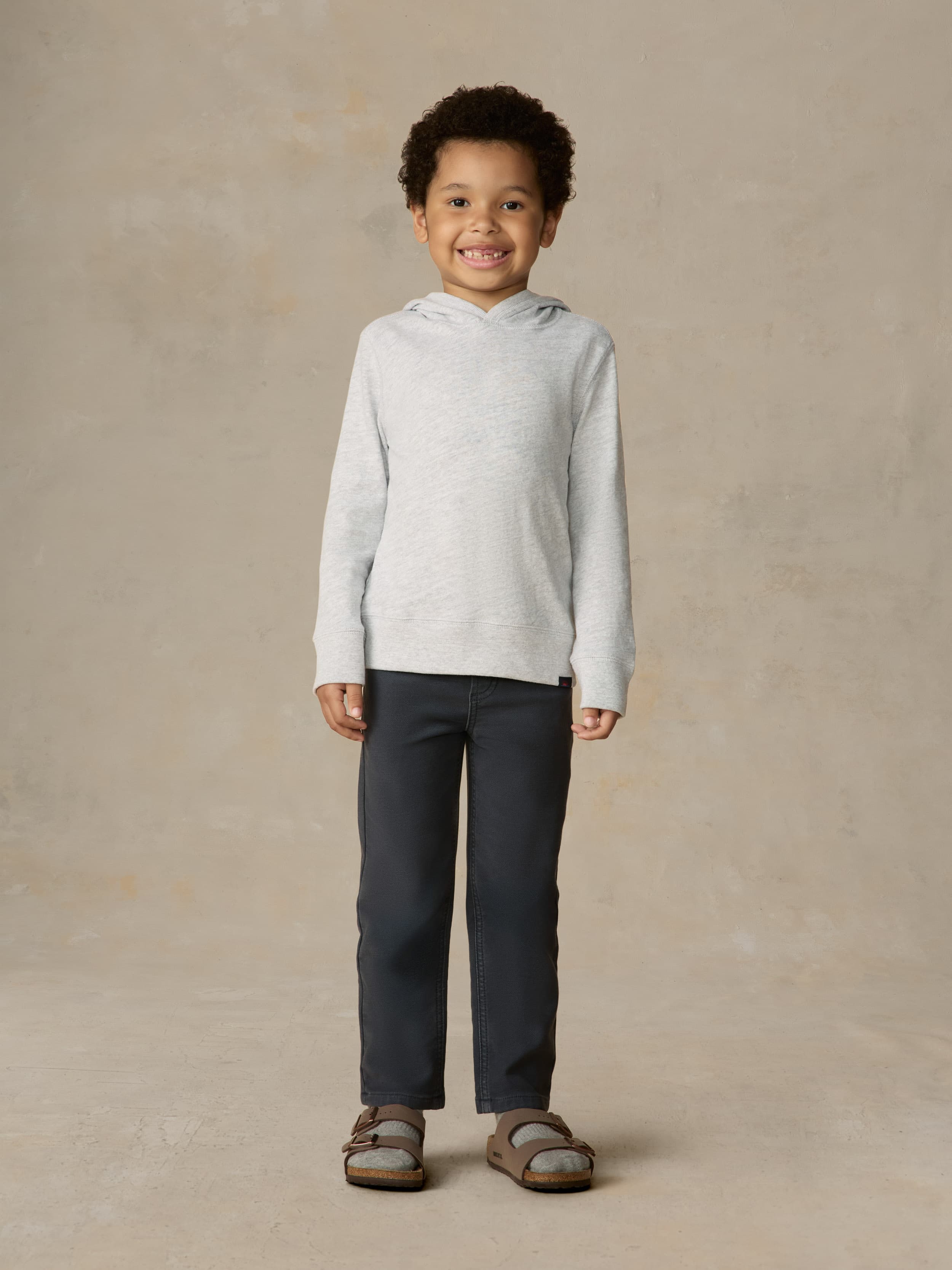 Child wearing a grey hoodie and navy pants against a beige background
