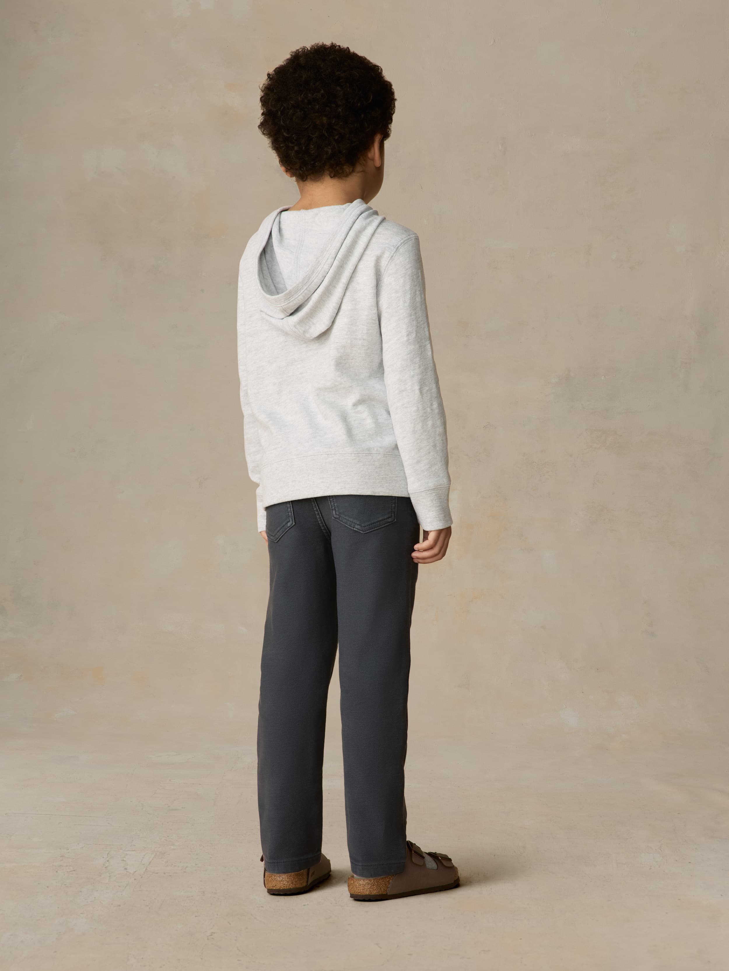 Child wearing a grey hoodie and navy pants against a beige background