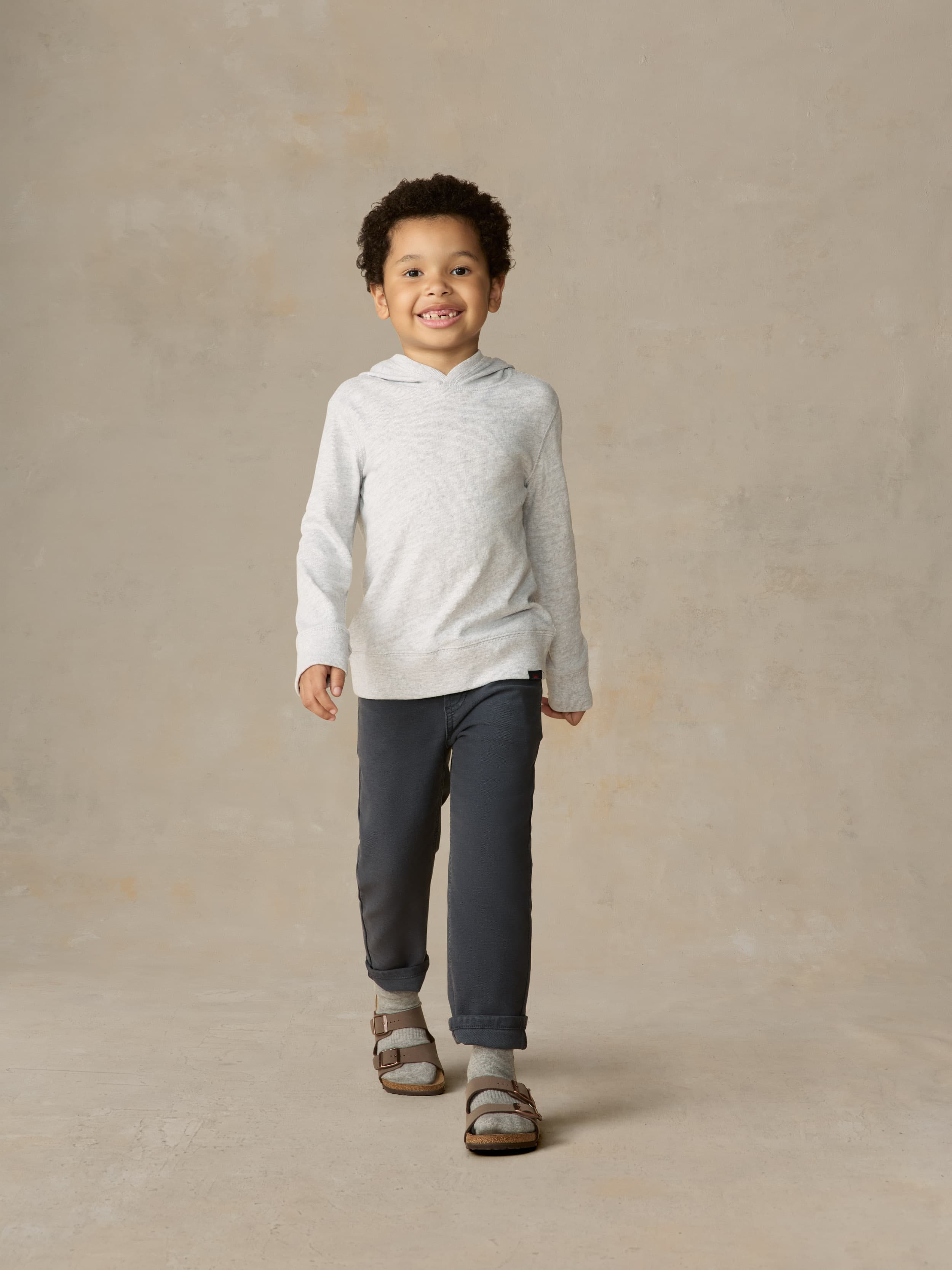Child wearing a grey hoodie and navy pants against a beige background