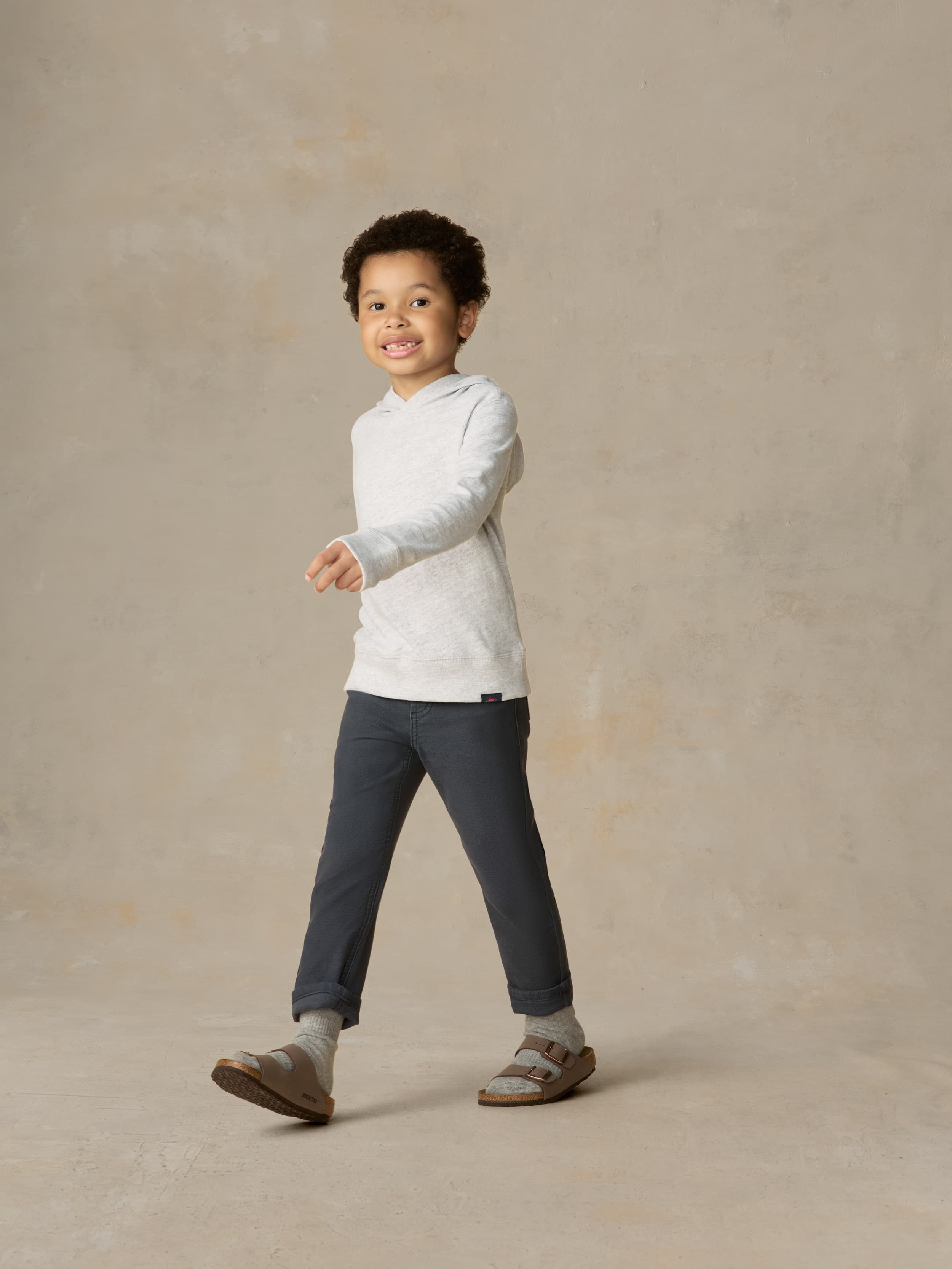 Child wearing a grey hoodie and navy pants against a beige background