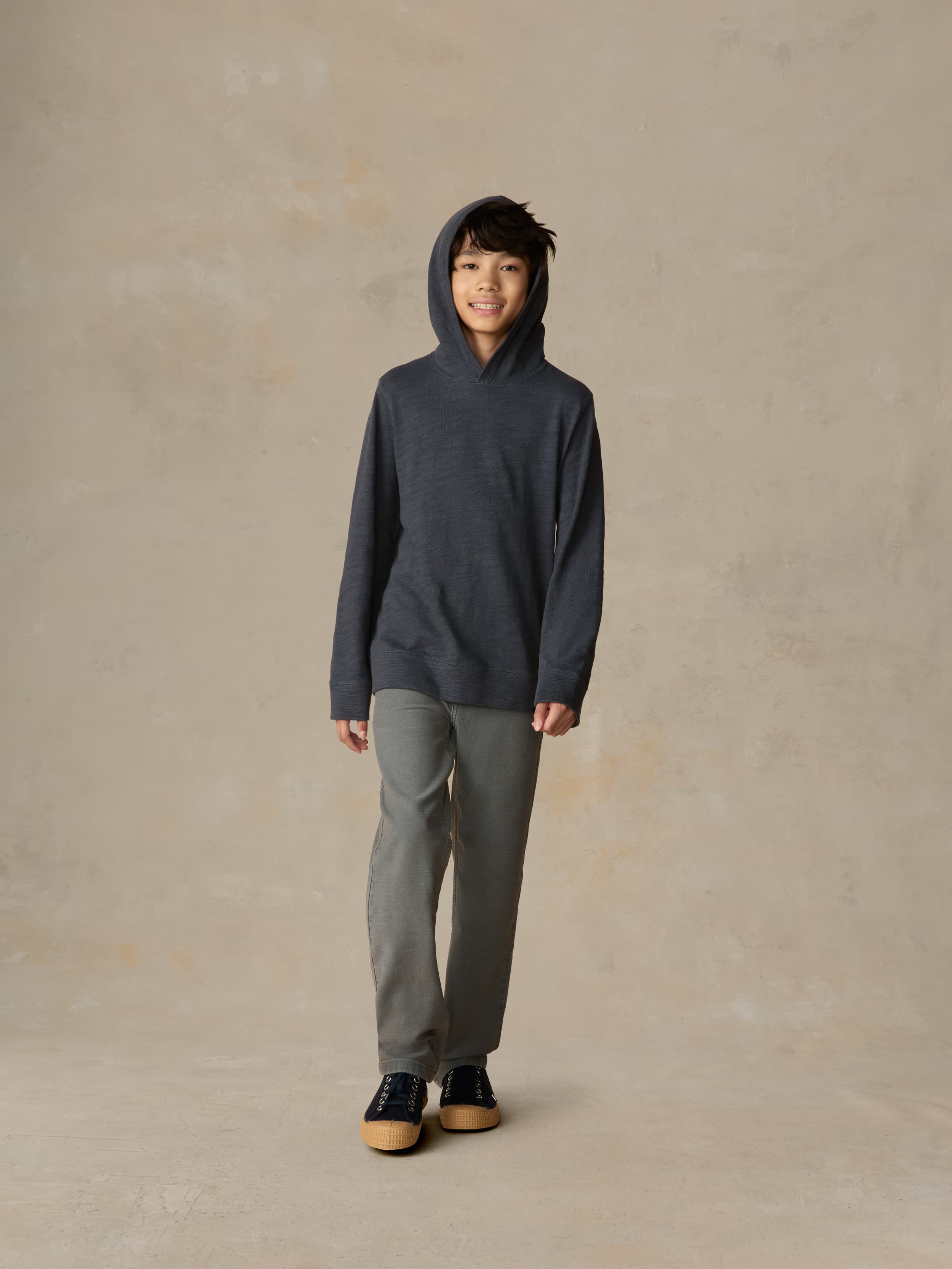 Child wearing a navy hoodie and grey pants against a beige background