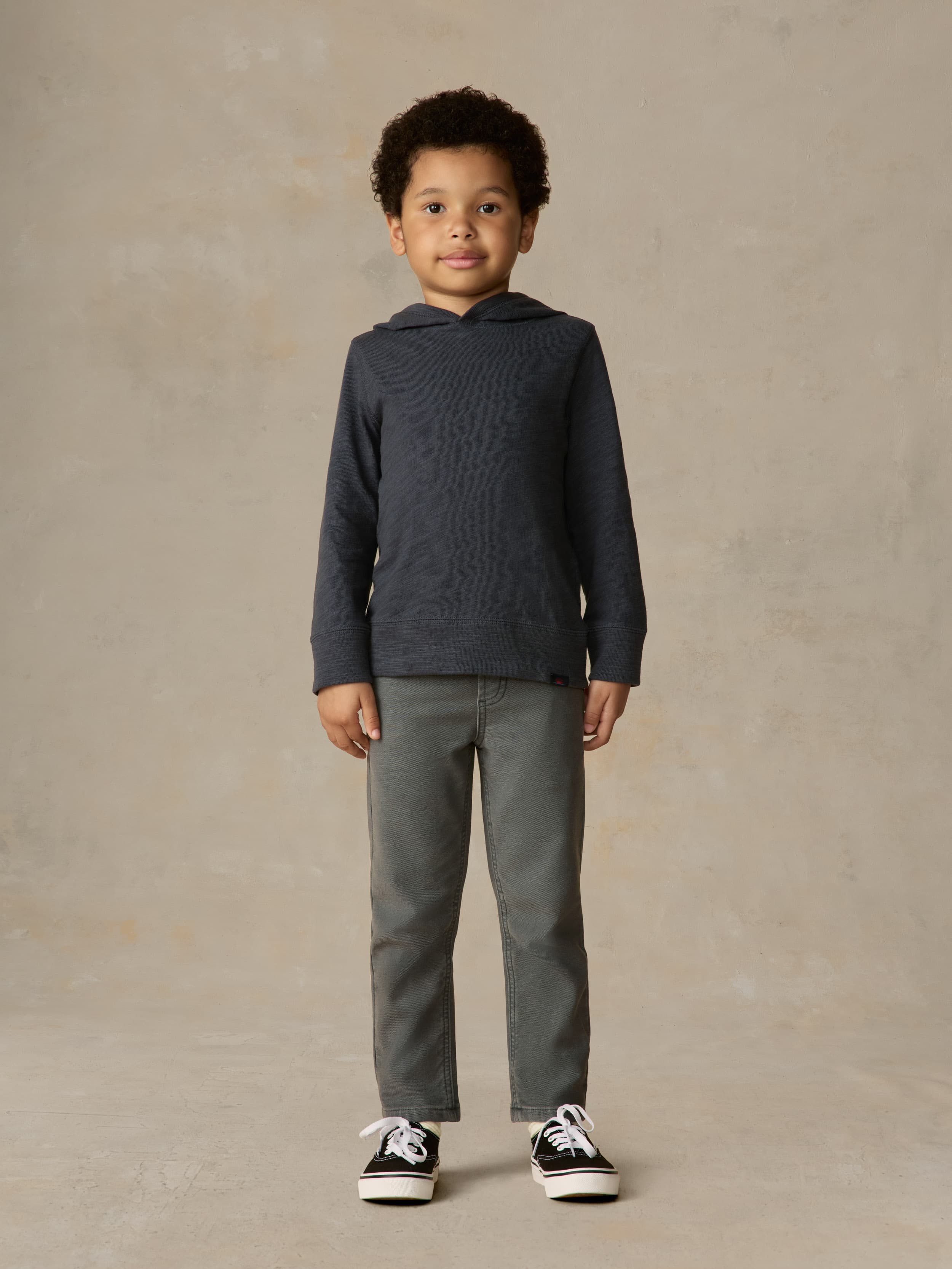Child wearing a navy hoodie and grey pants against a beige background