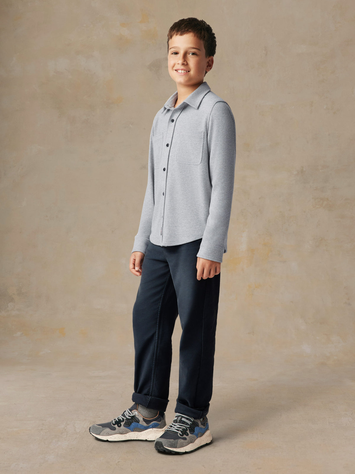 A child wearing a grey button up shirt and black pants, image 5 of 7