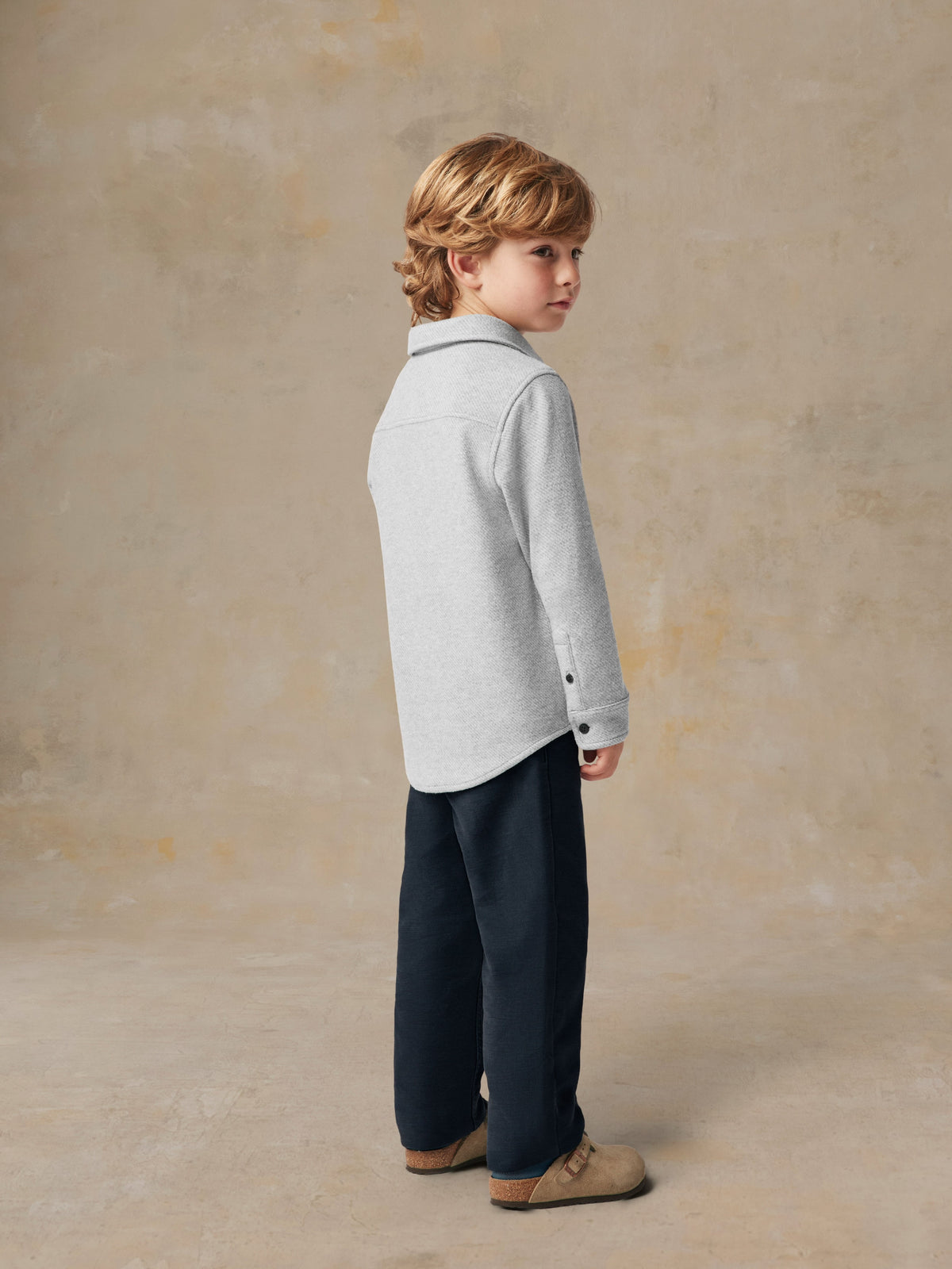 A child viewed from behind wearing a grey button up shirt and black pants, image 5 of 6